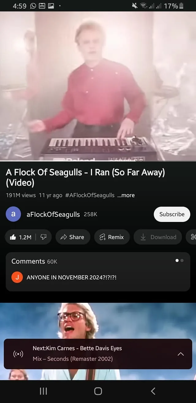 A band member is performing in a music video, playing a synthesizer keyboard. The individual is wearing a bright red shirt and appears to be in a foggy, illuminated setting, which gives a dreamy atmosphere. The background is somewhat obscured, but there are hints of other figures and reflective surfaces. The video is titled "A Flock Of Seagulls - I Ran (So Far Away)" and has garnered 191 million views. Below the video, there are comments, including one asking if anyone is present in November 2024. The video also features a suggestion for another song, "Kim Carnes - Bette Davis Eyes." The visible brand on the keyboard is "Roland."