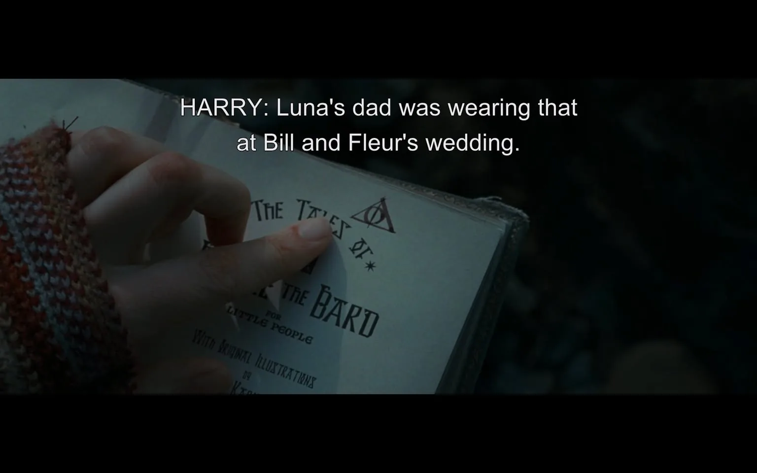 In the scene, a hand is seen holding an open book, with a focus on the page displaying the title "The Tales of Beedle the Bard." The hand appears to be wearing a knitted, multicolored sweater, suggesting a cozy or casual setting. The text on the page includes a decorative symbol resembling a triangle with a circle, which is associated with the story's themes. The dialogue attributed to Harry mentions Luna's dad and a wedding, indicating a narrative context related to characters from a fantasy series. The background is dimly lit, hinting at an outdoor or intimate setting, but no specific details about the environment are visible.