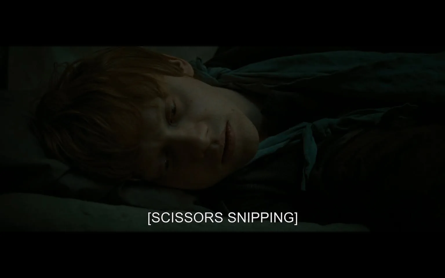 In the scene, a young man lies on a bed, appearing somewhat disheveled and introspective. His hair is tousled, and he has a faint expression of concern or contemplation on his face. He is dressed in dark clothing, with a scarf or piece of fabric draped around his neck. The setting is dimly lit, suggesting a somber or serious atmosphere. The text overlay indicates the sound of scissors snipping, hinting at an action occurring off-screen that may relate to the character's state of mind or situation. The overall mood is one of tension or unease, with the character seemingly lost in thought.