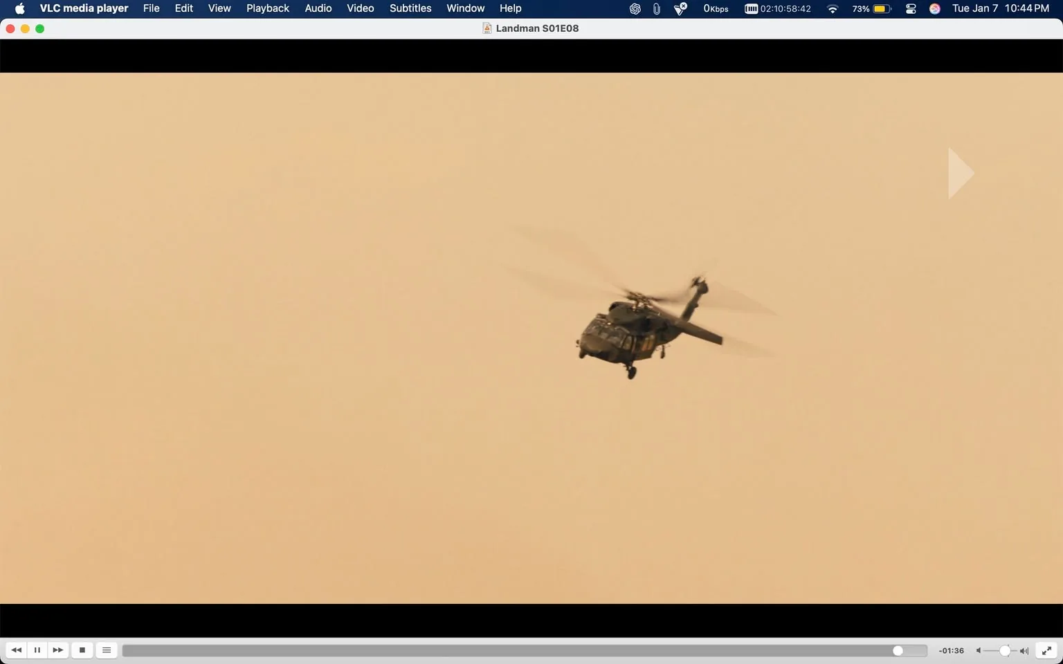 A helicopter is captured mid-flight, hovering against a backdrop of a muted, sandy-colored sky. The helicopter appears to be a military type, characterized by its robust design and rotor blades in motion. The image lacks any visible logos or brands. The overall atmosphere suggests a sense of urgency or action, typical of scenes involving helicopters. The background is devoid of any distinct features, emphasizing the helicopter as the focal point. There are no people or additional objects present in the frame, allowing the viewer to concentrate solely on the aircraft.