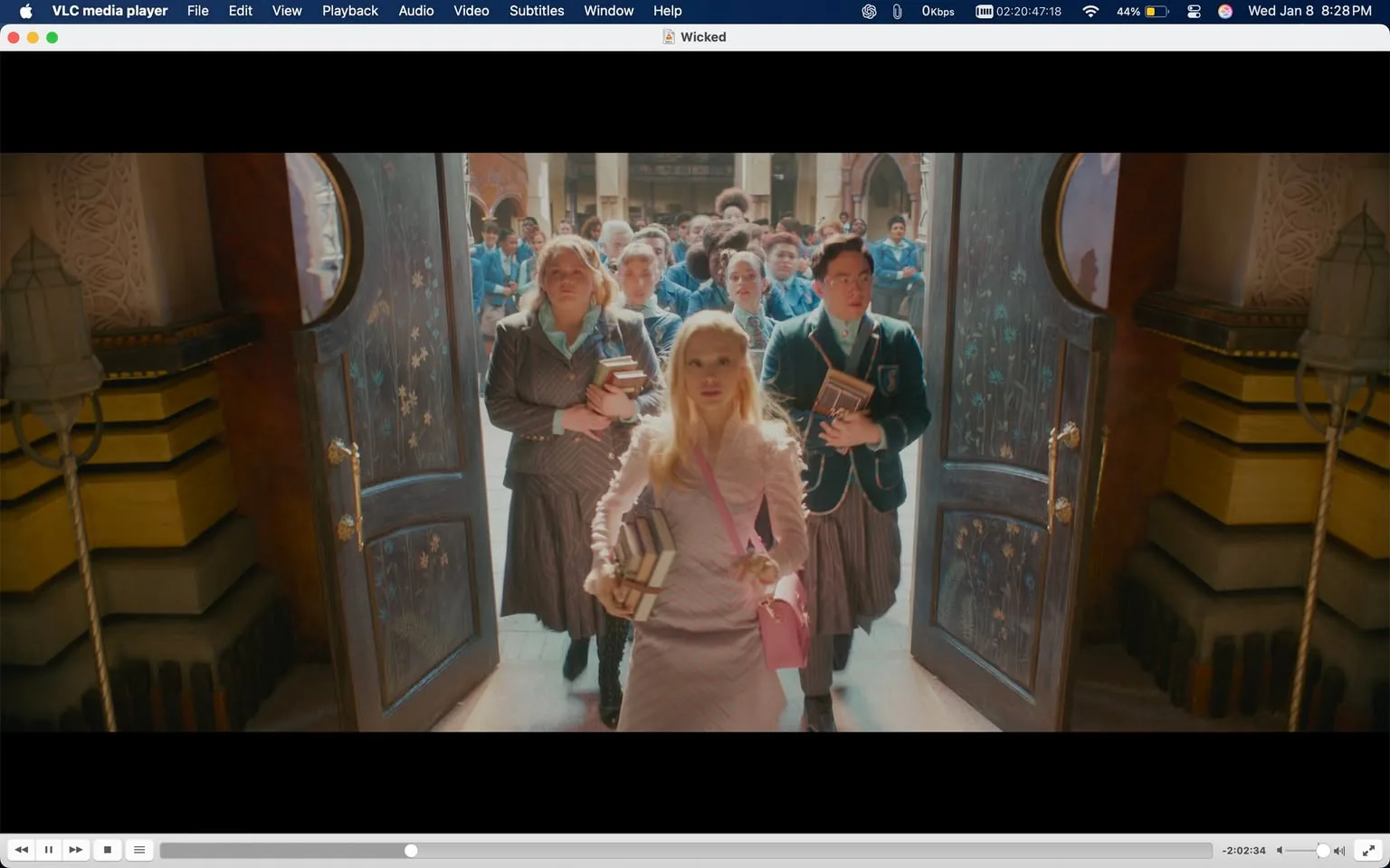In the scene, a group of students is exiting a grand building through large, ornate doors. The main focus is on a young woman in a light pink outfit, carrying several books and a pink handbag. She has long, wavy hair and appears to be in a confident pose. Surrounding her are other students, including a woman in a dark striped suit and a man in a green blazer, all holding books. The background features a vibrant crowd of students, suggesting a lively school environment. The architecture is detailed, with intricate designs visible on the doors and surrounding walls, indicating a fantastical setting. The lighting is bright, suggesting daytime.