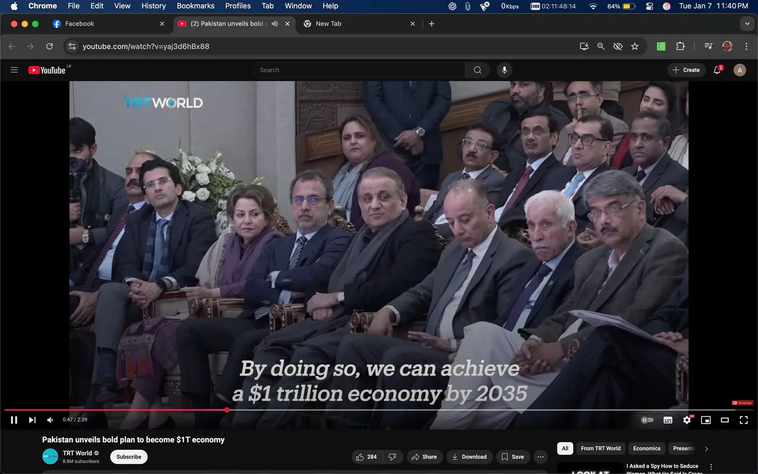 A group of individuals is seated in a formal setting, likely during a significant event or announcement. The scene features a diverse audience, with men and women dressed in business attire. Some individuals are engaged in listening attentively, while others appear to be in discussion. The background includes decorative elements, such as flowers, indicating a formal atmosphere. Prominently displayed on the screen is the logo "TRT World," suggesting the event may be covered by this media outlet. The visible text mentions achieving a "$1 trillion economy by 2035," indicating the topic of discussion. The overall mood appears serious and focused, reflecting the importance of the subject matter being addressed.