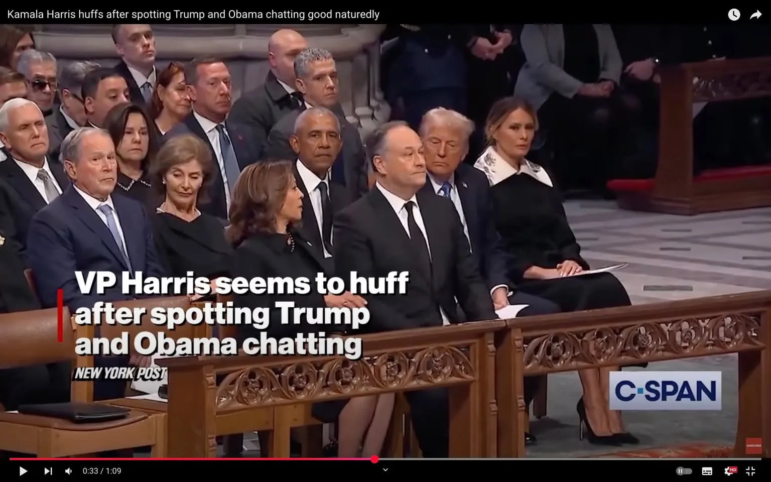 During a significant political event, several individuals are seated in a solemn setting, likely a memorial or funeral. Among them, an unidentified adult woman appears to express discontent, huffing as she observes two other individuals engaged in conversation. The scene captures a mix of emotions, with some attendees appearing serious while others are more relaxed. The individuals are dressed in formal attire, predominantly in dark colors, reflecting the somber nature of the occasion. The background features ornate wooden benches and a spacious interior, typical of a formal gathering space. A logo for C-SPAN is visible in the lower corner, indicating the event is being broadcast.