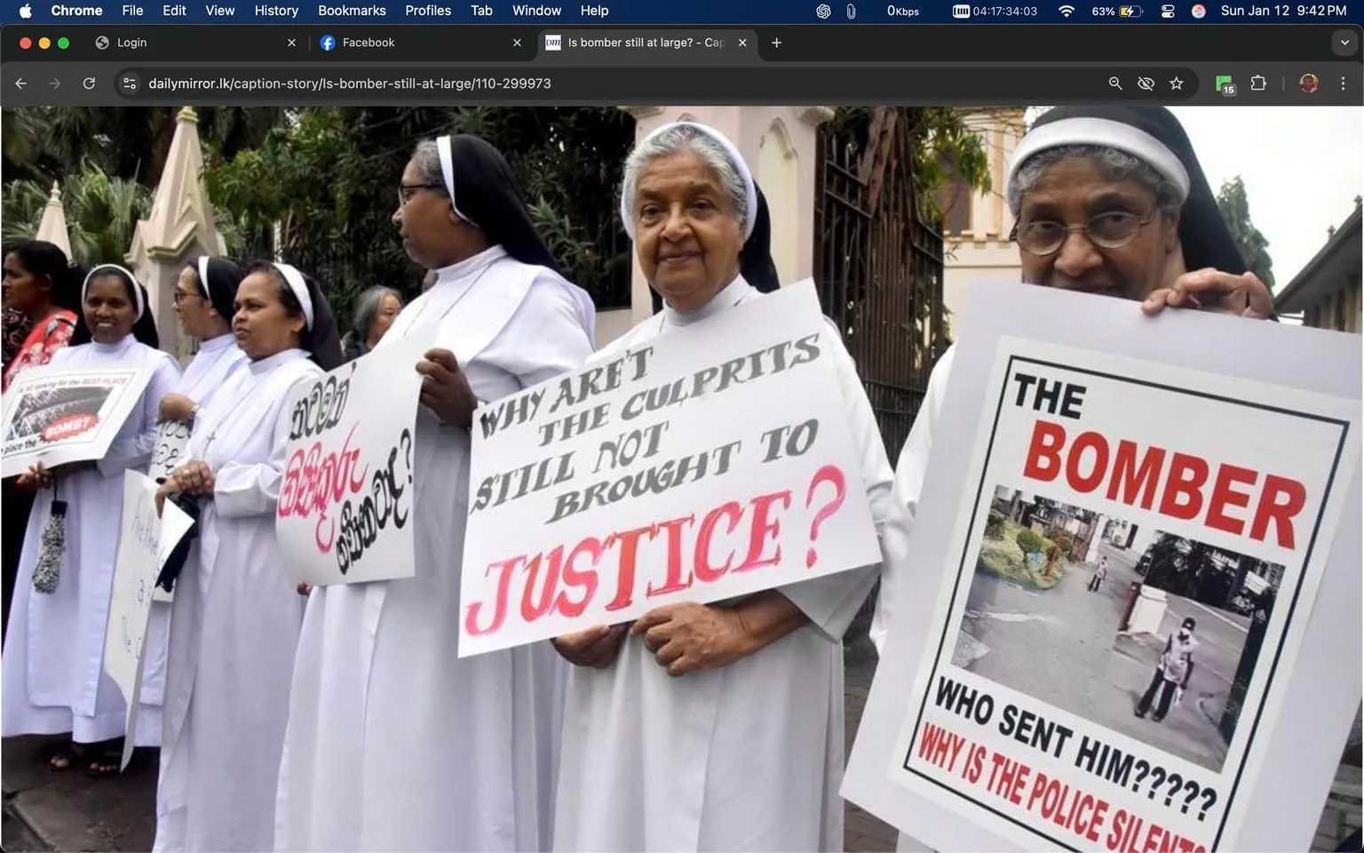A group of individuals, primarily dressed in white religious attire, is participating in a protest. They are holding signs with messages demanding justice and questioning the authorities. One sign reads, "WHY AREN'T THE CULPRITS STILL NOT BROUGHT TO JUSTICE?" in bold letters, while another sign states, "THE BOMBER" along with a photo and questions about the police's response. The setting appears to be outdoors, likely in a public space, with trees and a building visible in the background. The expressions of the participants convey a sense of urgency and concern regarding the issues they are addressing.