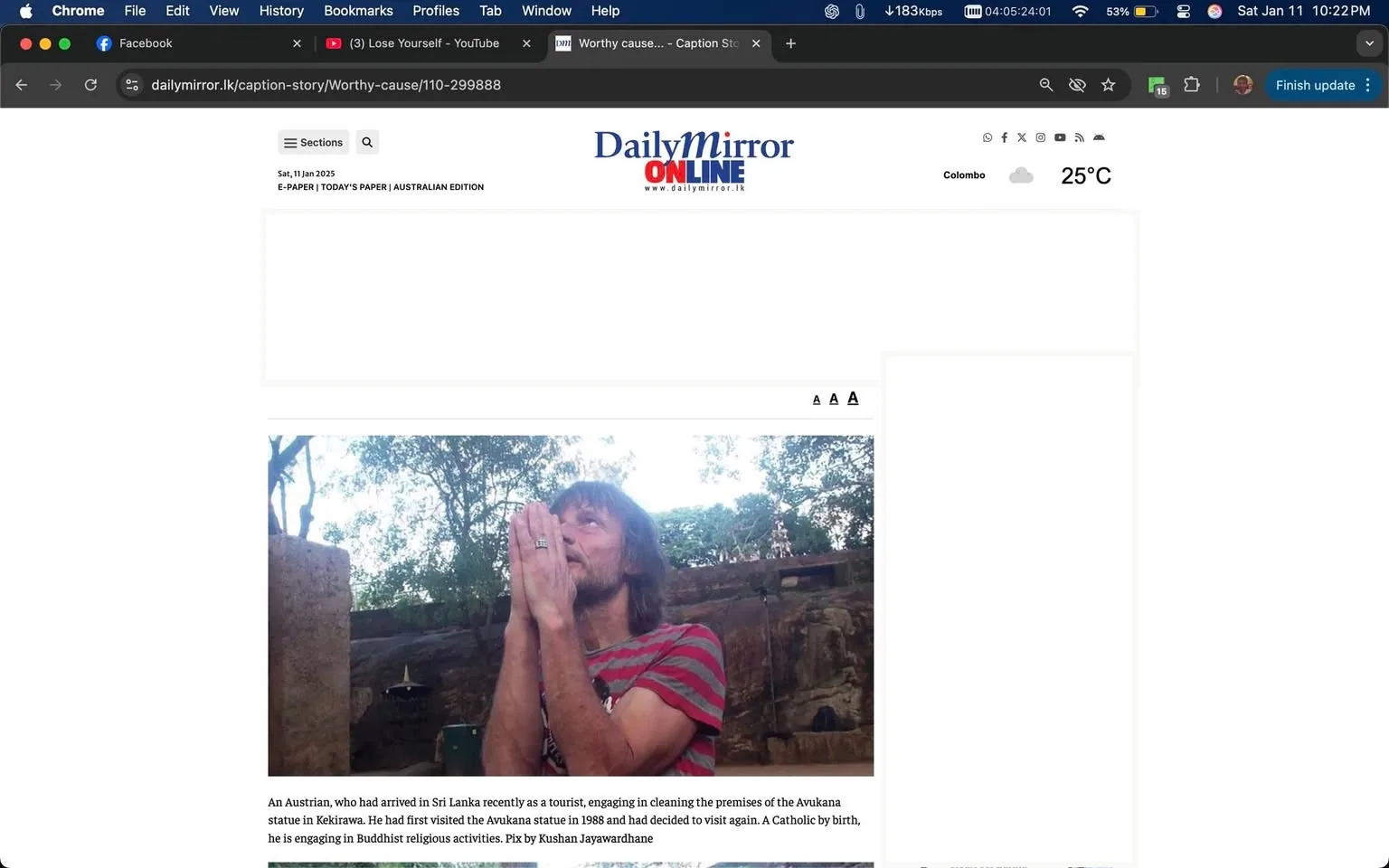 An unidentified adult male is seen with his hands clasped together in a prayer-like gesture, appearing to engage in a religious activity. He has long hair and is wearing a red and white striped shirt. The background features greenery and a stone structure, suggesting an outdoor setting, likely near a religious site. The article mentions that he is an Austrian tourist in Sri Lanka, involved in cleaning the premises of the Avukana statue, and has previously visited this site in 1988. The date on the article is January 10, 2025, and it includes a caption indicating the photo was taken by Kushan Jayawardhane.