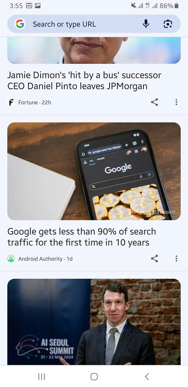 In the image, there are three news articles displayed on a mobile device screen. The first article discusses Jamie Dimon's successor, Daniel Pinto, leaving JPMorgan, with the source attributed to Fortune. The second article from Android Authority highlights that Google has received less than 90% of search traffic for the first time in a decade. The visible text includes the Google logo on a dark background, with a search bar and images of gold coins or tokens beneath it. The third article features a man in a suit, standing in front of a backdrop for the AI Seoul Summit, scheduled for May 2024. The setting appears to be indoors, with a brick wall visible in the background.