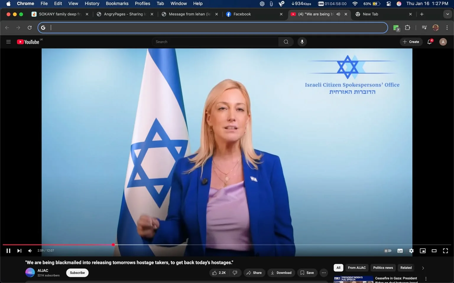 In the image, a speaker stands in front of a light blue background, flanked by an Israeli flag featuring a blue Star of David. The speaker, dressed in a blue blazer over a light purple top, appears to be delivering a message regarding a serious issue, as indicated by the text overlay that mentions being blackmailed into releasing hostage-takers. The setting suggests a formal communication, likely aimed at an audience concerned with current events. The logo of the Israeli Citizen Spokespersons' Office is visible in the upper right corner, reinforcing the official nature of the message. The speaker's expression is serious, reflecting the gravity of the topic being discussed.