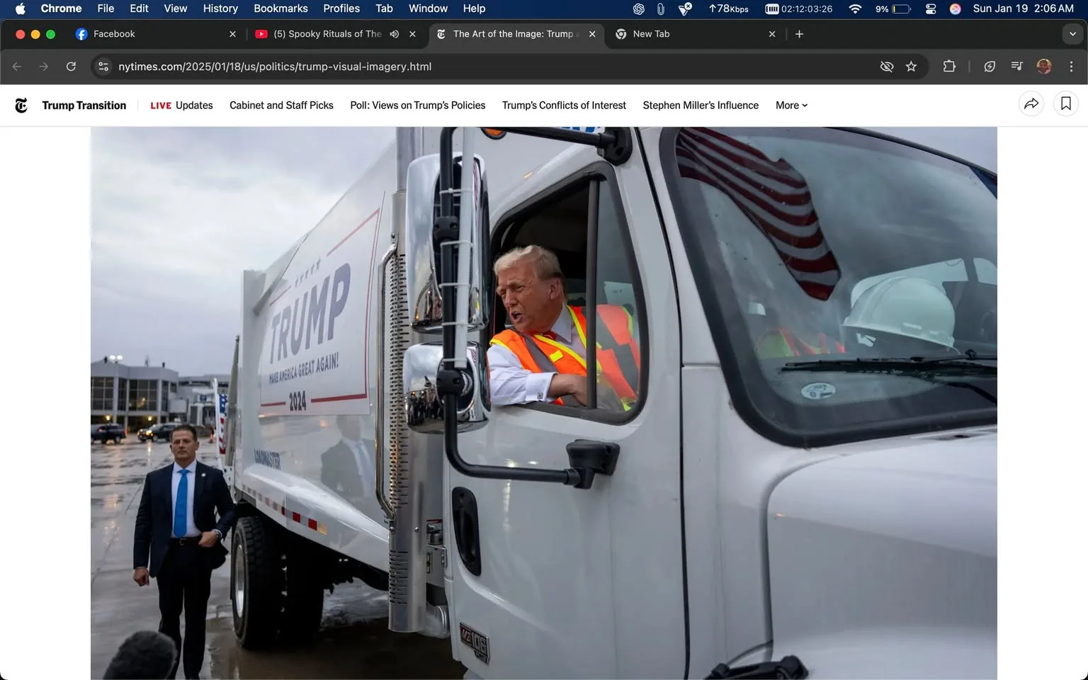 A person is seated in the driver's seat of a large white truck, which has visible political branding that reads "TRUMP" and "MAKE AMERICA GREAT AGAIN! 2024." The individual appears to be wearing an orange safety vest over a white shirt, and they are leaning out of the window, seemingly engaged in conversation or expressing an emotion. The setting is outdoors, with a cloudy sky suggesting it might be early morning or late afternoon. In the background, there are vehicles parked and a building that appears to be part of a commercial area. An American flag is reflected in the truck's window, adding to the political context of the scene.