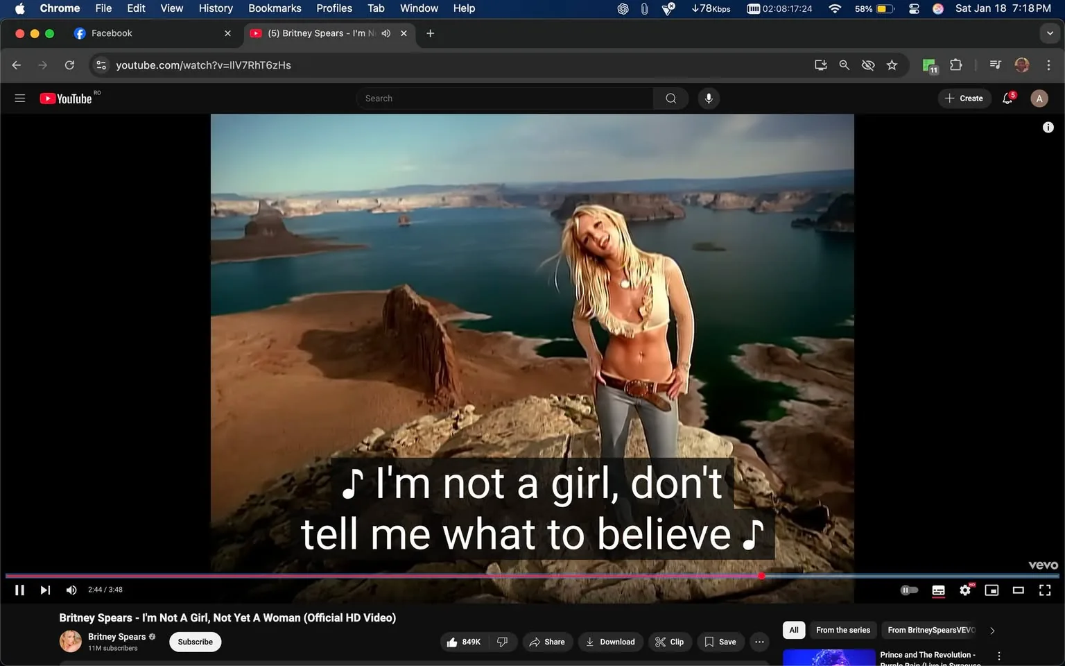 In the image, an unidentified adult stands on a rocky outcrop overlooking a large body of water, surrounded by a dramatic landscape of cliffs and hills. The person has long, blonde hair and is wearing a light-colored, revealing top paired with blue jeans. They appear to be posing playfully, with a slight smile on their face. The background features a serene lake with a calm surface, reflecting the sky, and the scene is set in a natural outdoor environment, likely during daylight. The text overlay includes lyrics from a song, emphasizing themes of identity and self-expression. There are no visible brands or logos in the image.