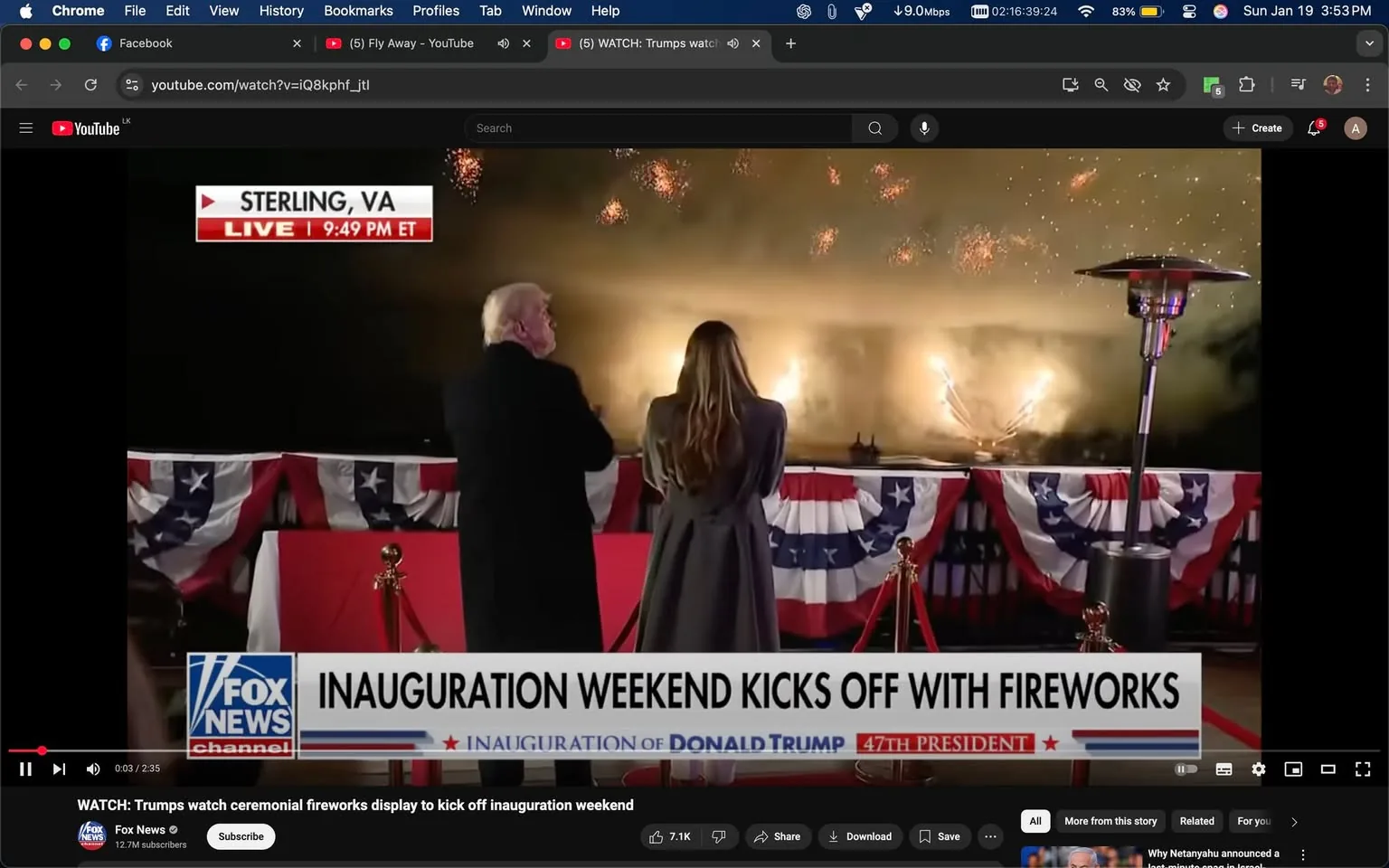 In the image, two individuals are watching a fireworks display, which is part of an inauguration weekend event. The setting appears to be outdoors in Sterling, Virginia, during the evening, as indicated by the dark sky illuminated by fireworks. The individuals are standing side by side, with one wearing a black coat and the other in a long gray coat. They are both facing the fireworks, which are bursting in the sky, creating a vibrant display of colors against the backdrop of smoke. 

The foreground features a red carpet and decorative elements, including patriotic bunting in red, white, and blue, suggesting a celebratory atmosphere. A heater is visible nearby, indicating it might be chilly. The screen displays a banner from Fox News, indicating the live broadcast of the event, with the time noted as 9:49 PM ET. The text mentions the inauguration weekend, specifically referencing Donald Trump as the 47th President. The overall mood is festive, marked by the excitement of the fireworks and the significance of the occasion.