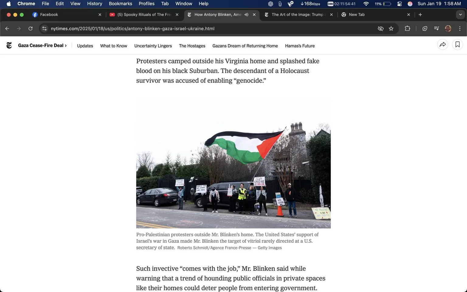 Protesters gathered outside a residence in Virginia, demonstrating against U.S. Secretary of State Antony Blinken. The scene features a group of individuals holding signs with messages related to their cause, which appears to be pro-Palestinian in nature. A prominent flag, likely representing Palestine, is being waved, showcasing the colors black, red, green, and white. The protesters are dressed in casual clothing, with some wearing jackets and reflective vests, indicating a level of organization. 

The setting is outdoors, with a suburban backdrop that includes a large, possibly historic house and well-maintained greenery. The time of day appears to be overcast, suggesting a cooler climate. The vehicles parked nearby include a black SUV, which is splattered with what seems to be fake blood, symbolizing the protesters' message. The signs held by the protesters contain various slogans, some of which are legible, expressing their discontent with Blinken's policies. Overall, the atmosphere conveys a sense of urgency and activism, with the protesters visibly engaged in their demonstration.