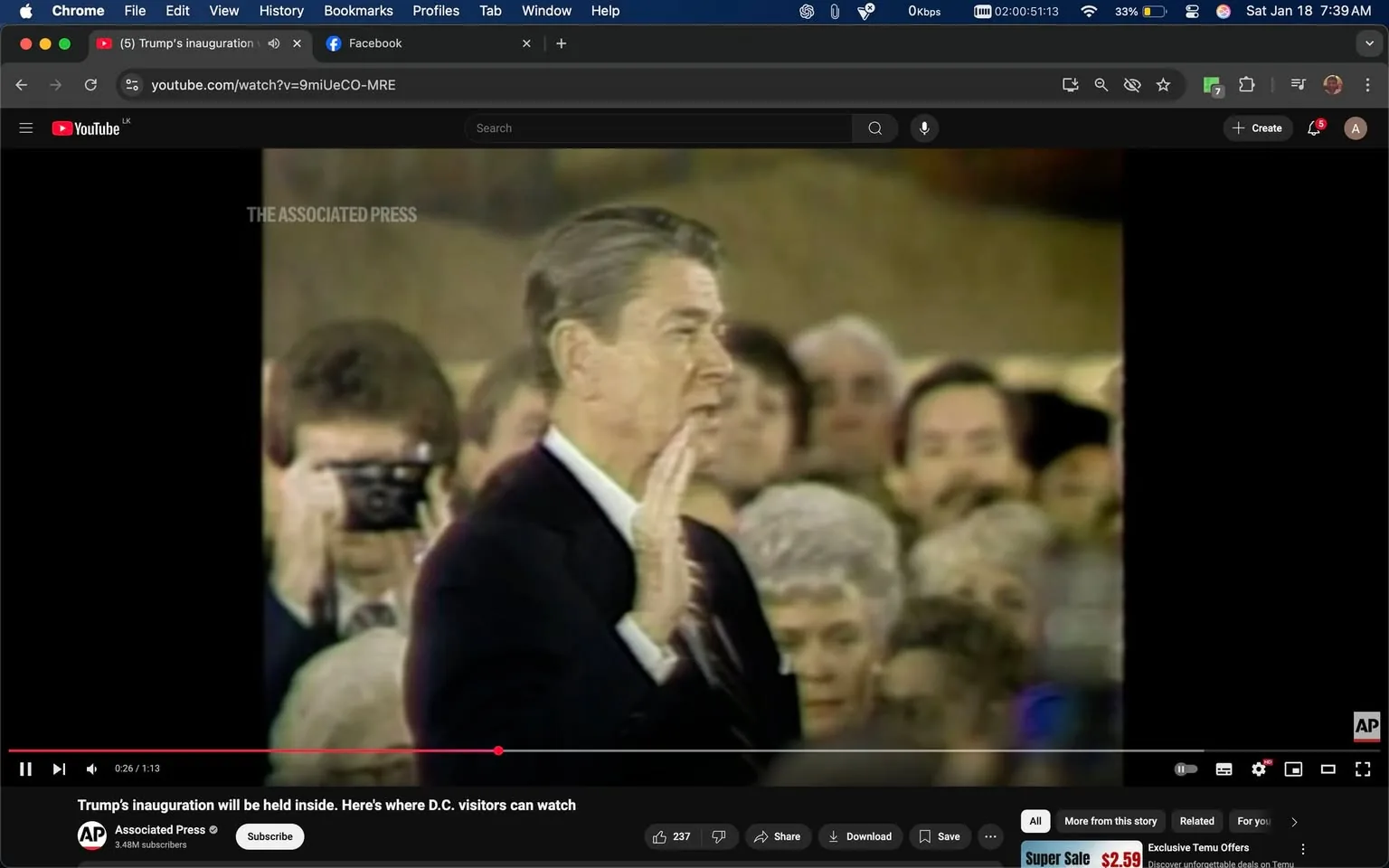 During a notable event, a man is seen raising his right hand, appearing to take an oath or make a pledge. He is dressed in a dark suit with a white shirt and tie. The background is filled with a crowd of people, some of whom are looking directly at him, while others appear to be engaged in conversation or watching intently. A person in the foreground is holding a camera, capturing the moment. The setting appears to be indoors, likely at a formal ceremony, with a blurred backdrop that suggests a large gathering. The text "THE ASSOCIATED PRESS" is visible, indicating the source of the image. The overall atmosphere is serious and ceremonial, reflecting the significance of the occasion.