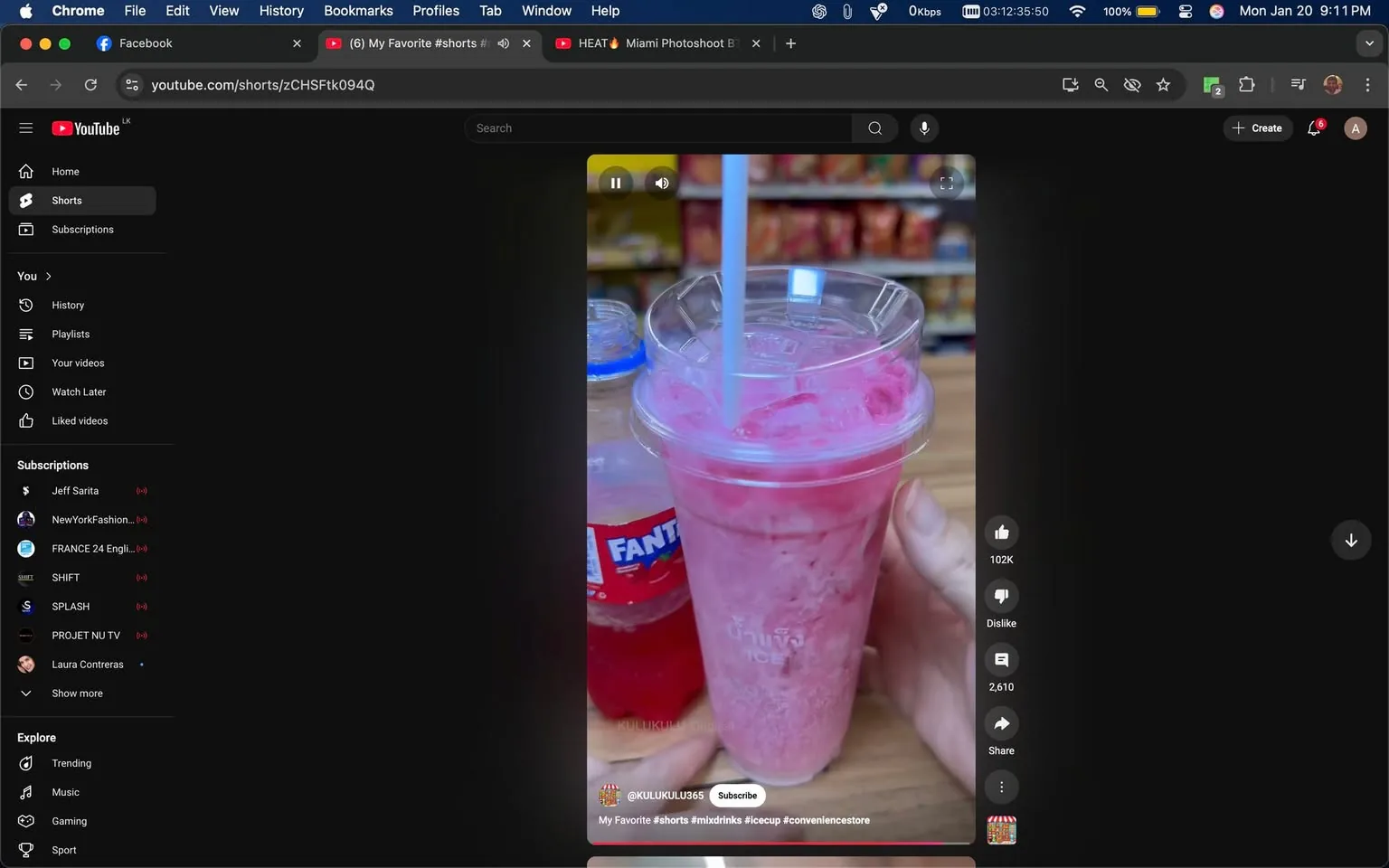 In the image, a hand is holding a clear plastic cup filled with a pink drink, which appears to be a slushy or blended beverage, topped with ice and a straw. The drink has a vibrant pink color, suggesting it may be fruit-flavored. Next to this cup is a bottle of Fanta, a well-known soft drink brand, featuring a red liquid inside. The bottle has a prominent label with the Fanta logo, which is easily recognizable. The background shows shelves stocked with various products, indicating that this scene is likely set in a convenience store or a similar retail environment. The lighting is bright, suggesting an indoor setting, and the overall atmosphere appears casual and inviting. There are no visible people in the image, focusing solely on the drinks.
