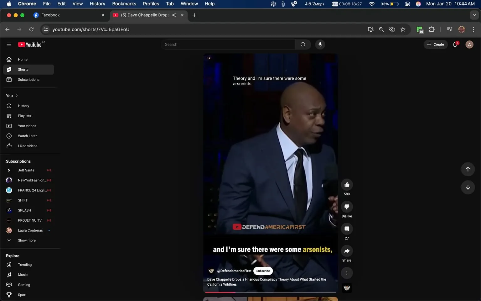 In the image, a comedian is performing on stage, wearing a dark suit with a white shirt and a black tie. He is speaking into a microphone, appearing animated and engaged with the audience. The background is dimly lit, with blue lighting that creates a dramatic atmosphere. The text overlay includes a humorous statement about conspiracy theories and arsonists, suggesting that the content is comedic in nature. The video appears to be a clip from a performance, likely intended for social media sharing, as indicated by the platform interface visible around the video. The overall setting suggests a live comedy show, with the audience likely present, although they are not visible in the frame. The focus is on the comedian's expression and delivery, which conveys humor and engagement.
