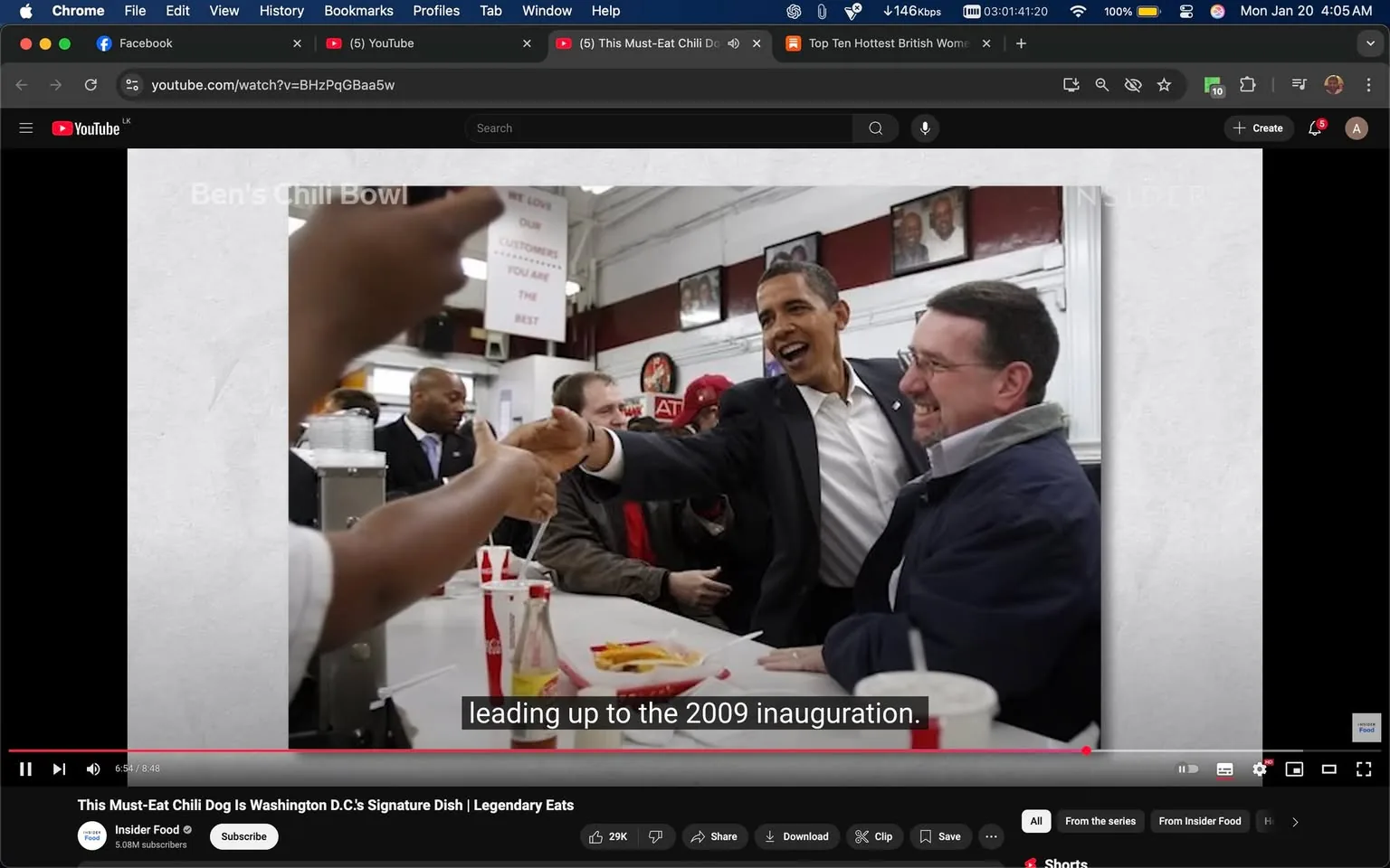 In the image, a man, likely a public figure, is seen smiling and shaking hands with another individual in a lively indoor setting, possibly a restaurant. The man appears to be wearing a suit and has a cheerful expression, suggesting a friendly interaction. The other person, dressed in a blue jacket with a light-colored collar, is also smiling, indicating a positive exchange. 

In the background, there are several people, including a man in a suit and a woman wearing a hat, all engaged in conversation. The setting features a counter with food items, including what looks like fries and drinks, possibly from a fast-food establishment. A sign on the wall reads, "WE LOVE OUR CUSTOMERS YOU ARE THE BEST," adding to the welcoming atmosphere. 

The visible logo on a cup suggests it is a Coca-Cola drink. The overall scene appears to be casual and celebratory, likely during a significant event, as indicated by the context of the 2009 inauguration mentioned in the subtitles.