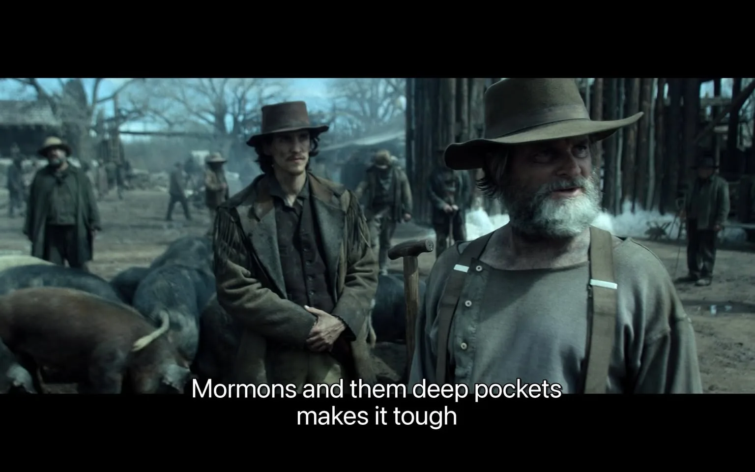 In the scene, a group of men is gathered outdoors, surrounded by livestock, likely in a rural or frontier setting. The atmosphere appears tense, with a focus on two main figures in the foreground. One man, dressed in a rugged coat with fringe details, stands with a serious expression, while another man, older with a beard, speaks animatedly. He wears a simple shirt and suspenders, suggesting a working-class background. The dialogue displayed at the bottom references "Mormons and them deep pockets," hinting at economic or social struggles. The background features other men engaged in various activities, with trees and structures visible, indicating a community or settlement. The overall tone suggests themes of hardship and conflict.