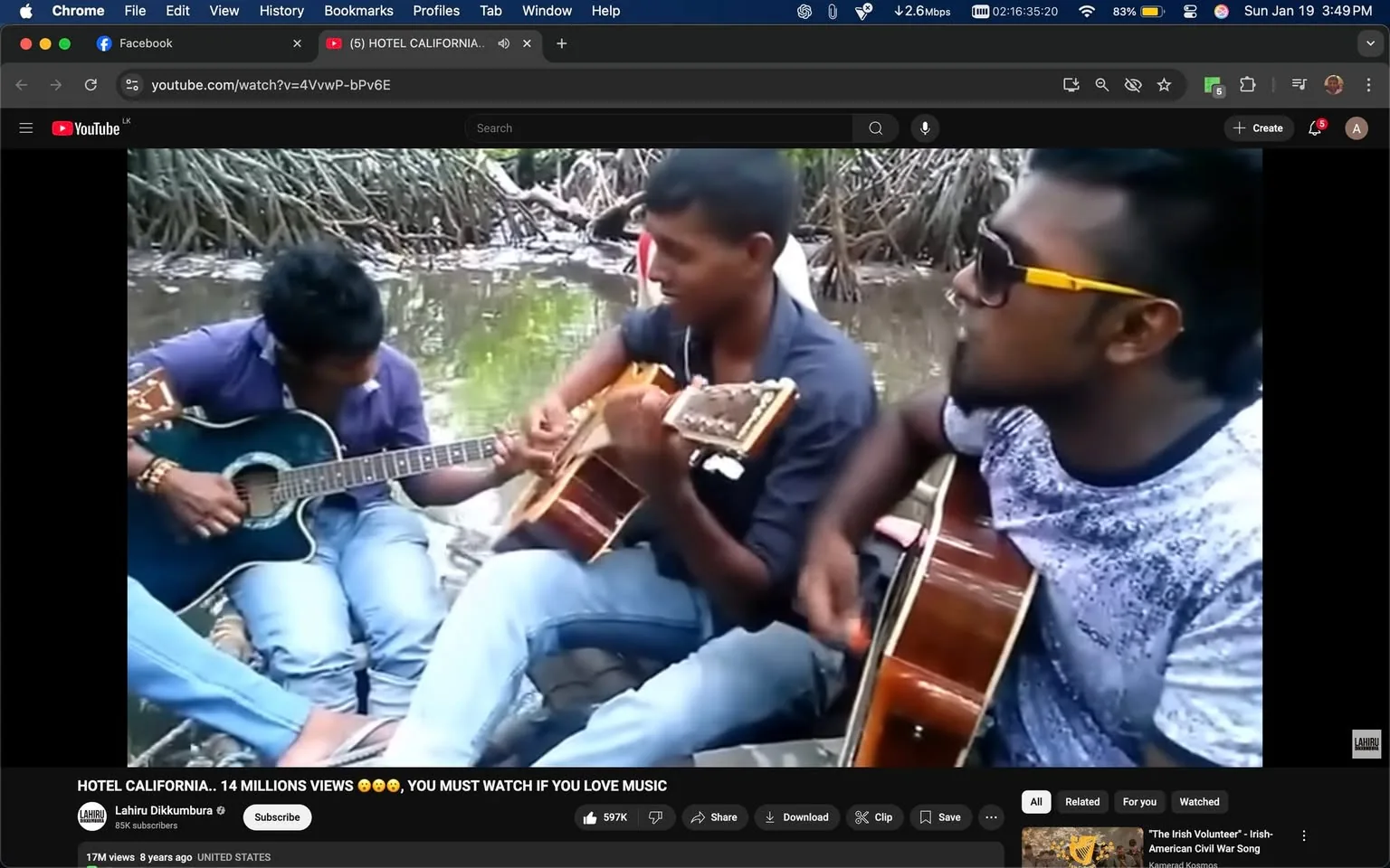 The scene features three young men gathered by a body of water, engaged in playing acoustic guitars. One individual on the left is playing a blue guitar, while another in the center holds a brown guitar. The third person, on the right, is also playing a guitar and wearing sunglasses with yellow accents. They appear to be enjoying a casual jam session, likely outdoors in a natural setting, surrounded by greenery and mangroves in the background. The atmosphere seems relaxed and informal, suggesting they are sharing a moment of music together. The individuals are dressed in casual clothing, with jeans and t-shirts, and their expressions indicate concentration and enjoyment as they play. There are no visible signs of violence, sexual content, or any brands present in the image.