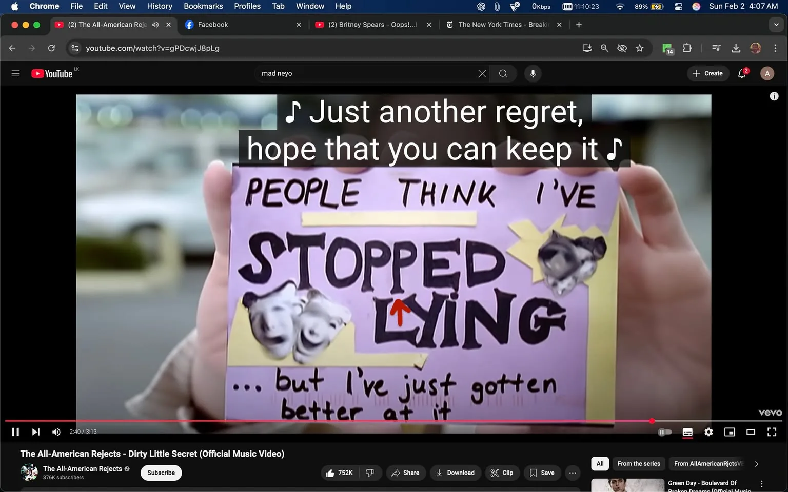 In the image, a person is holding a colorful sign that reads, "PEOPLE THINK I'VE STOPPED LYING ... but I've just gotten better at it." The sign is predominantly purple with bold black lettering, and it features cut-out images of faces, possibly expressing various emotions. The background appears to be an outdoor setting, likely a parking lot, with blurred vehicles and soft lighting suggesting it could be daytime. The person holding the sign is partially visible, showing a hand and part of an arm, but their face is not shown. The scene is likely from a music video, as indicated by the visible lyrics at the top of the image, which include the lines, "Just another regret, hope that you can keep it." The overall atmosphere conveys a sense of introspection and emotional expression, typical of music video themes.