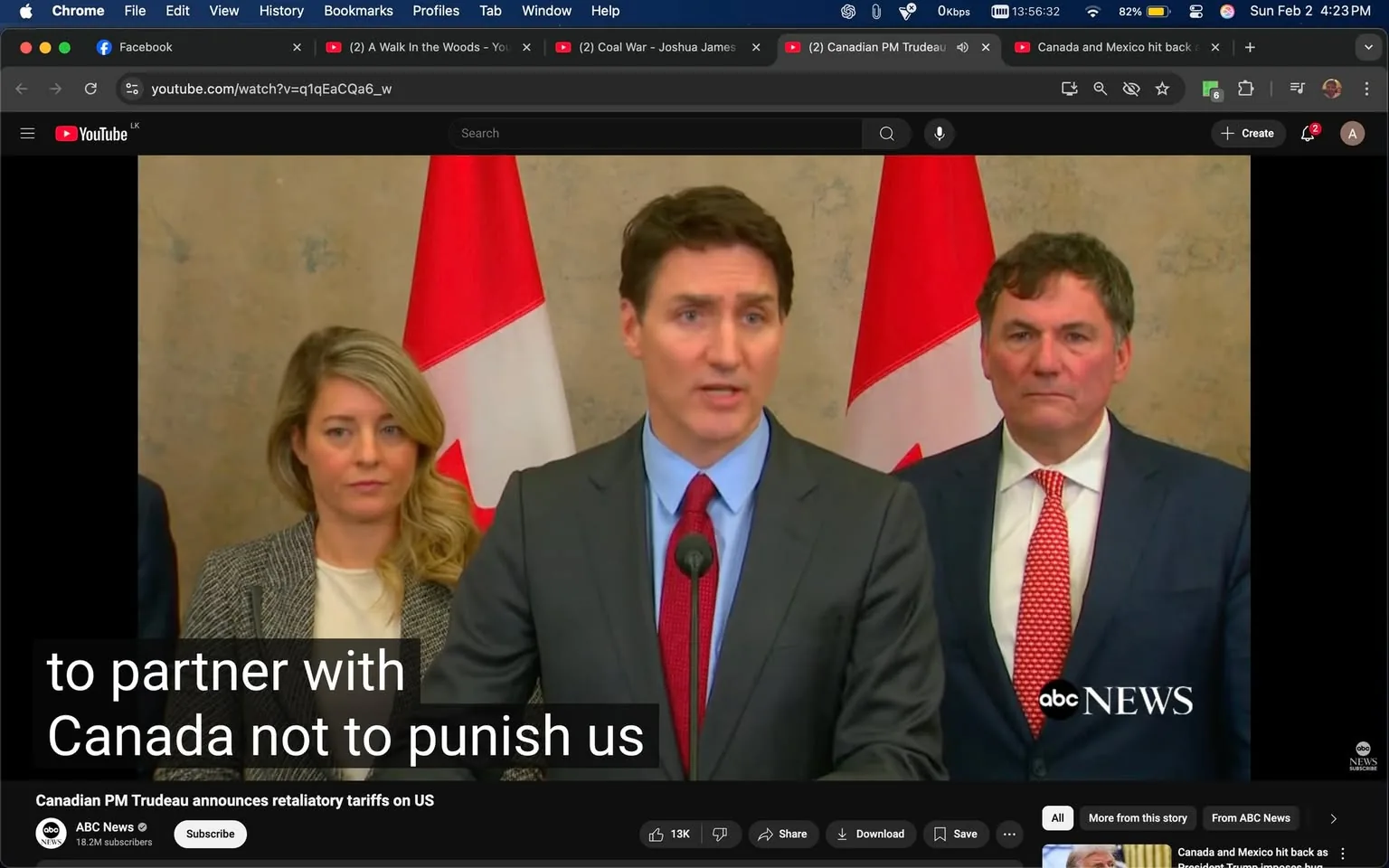 In the image, a political figure is speaking at a podium, flanked by two others. The main speaker, dressed in a dark suit with a light blue shirt and a red tie, appears to be addressing an audience, likely discussing a political issue. Behind him, two Canadian flags are prominently displayed, indicating the setting is likely a formal announcement or press conference in Canada. 

To his left, a woman with long, wavy blonde hair is wearing a black and white patterned blazer. She has a serious expression, suggesting she is engaged in the discussion. To the right of the main speaker stands another man in a dark suit with a white shirt and a red patterned tie, who appears to be listening attentively. 

The background is neutral, with a textured wall that does not distract from the speakers. The visible text at the bottom indicates that the announcement pertains to retaliatory tariffs on the U.S., hinting at a tense political situation. The overall atmosphere is formal and serious, typical of a governmental press conference.
