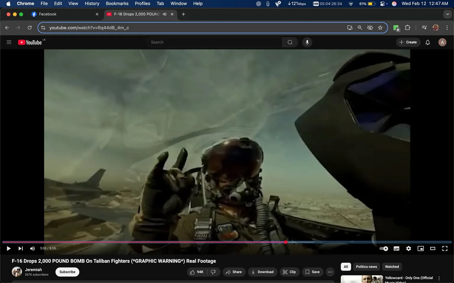 The image depicts a cockpit view from a military aircraft, likely an F-16 fighter jet. In the foreground, a pilot is visible, wearing a full-face helmet with a reflective visor that obscures their facial features. The pilot's gloved hand is raised in a gesture, possibly a peace sign or a "rock on" hand sign, indicating a casual or celebratory mood.

The pilot is dressed in a military flight suit, which is typically olive green or tan, and features various patches or insignia on the chest area, although the details of these patches are not clearly visible. The cockpit is equipped with various instruments and controls, which are partially visible in the lower part of the image. The cockpit's design includes a heads-up display (HUD) and other avionics typical of modern fighter jets.

In the background, the sky is visible, showcasing a mix of clouds and blue, suggesting a clear day. The landscape below appears to be arid, possibly desert terrain, with hints of structures or vehicles scattered across the ground, indicating a military operational area.

No readable text, logos, or trademarks are present in the image. The overall setting conveys a sense of action and military engagement, typical of aerial combat scenarios. The image captures a moment that reflects the pilot's experience in a high-stakes environment.