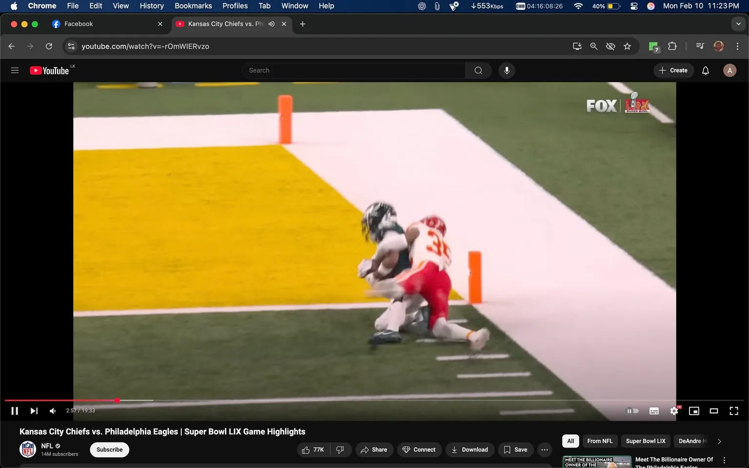 The image depicts a moment from a football game, specifically a highlight from the Super Bowl between the Kansas City Chiefs and the Philadelphia Eagles. 

In the foreground, two players are engaged in a play near the end zone. The player on the left, presumably from the Philadelphia Eagles, is wearing a dark green jersey with white accents and white pants. He is in a crouched position, reaching for the football, which he appears to be catching. His helmet is dark green, matching his jersey, and he is wearing white gloves. 

The player on the right, representing the Kansas City Chiefs, is wearing a white jersey with red and yellow accents, along with red pants. His jersey features the number 32. He is in a tackling position, attempting to stop the player from the Eagles. His helmet is white, and he has a determined stance as he reaches towards the player from the Eagles.

The background features a football field with a bright yellow end zone area, marked by a solid yellow section and a white boundary line. There are two orange goalposts visible at the back of the end zone. The field itself is a vibrant green, indicating a well-maintained playing surface.

In the upper right corner, there is a logo for FOX Sports, indicating the broadcast network. Below the image, there is a YouTube interface showing the video title "Kansas City Chiefs vs. Philadelphia Eagles | Super Bowl LIX Game Highlights," along with a play button and a progress bar indicating the video is at 2:57 out of 19:33 minutes. The video has 77K likes, and there are options to share, connect, and download.

Overall, the image captures a dynamic moment in a professional football game, highlighting the athleticism and competitive nature of the sport.