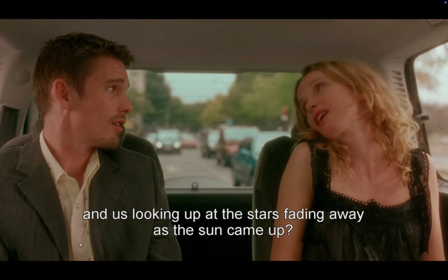 The image depicts two individuals seated in the back of a vehicle, likely a car, with a view of a street visible through the rear window. 

**People:**
1. **Male**: On the left side of the image, he has short, slightly tousled dark hair and is wearing a light-colored shirt under a dark suit jacket. His facial expression appears to be one of engagement or contemplation as he looks towards the female figure. 
2. **Female**: On the right side, she has long, wavy blonde hair and is wearing a black sleeveless top with lace detailing. Her posture is relaxed, leaning slightly back with her head tilted, suggesting a casual demeanor. She appears to be looking at the male figure, possibly in a moment of conversation.

**Text**: There is visible text at the bottom of the image, which reads: "and us looking up at the stars fading away as the sun came up?" This text is likely a quote from the dialogue in the scene.

**Setting**: The background shows a street lined with trees and parked cars, indicating an urban environment. The lighting suggests it is daytime, with soft natural light illuminating the interior of the vehicle.

**Overall Context**: The scene captures a moment of dialogue between the two individuals, with a focus on their expressions and the intimate setting of the car, which adds to the personal nature of their conversation.