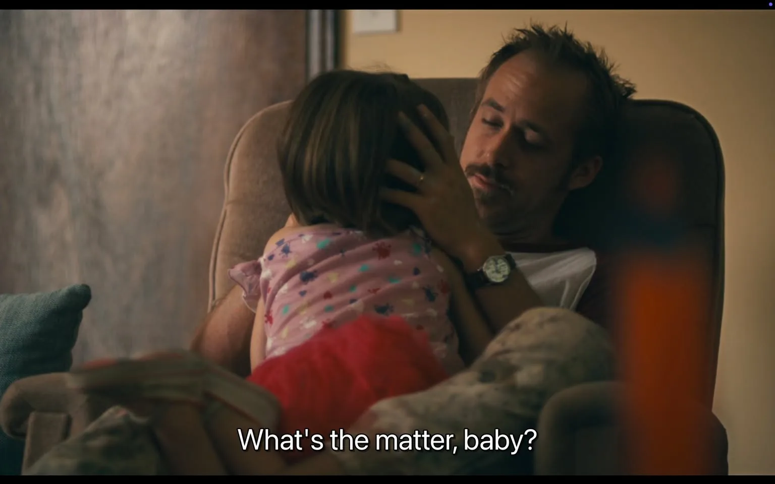 The image depicts a scene in a domestic setting, likely a living room. 

**Text:** At the bottom of the image, there is readable text that says, "What's the matter, baby?" This text appears to be a dialogue caption.

**People:** 
- There are two individuals present in the image:
  1. An adult male, who is seated in a chair. He has short, light brown hair and a mustache. He is wearing a white t-shirt with red sleeves and appears to be in a relaxed posture. His facial expression is calm and attentive as he looks at the child. He has a watch on his left wrist.
  2. A young girl, whose back is facing the camera. She has brown hair and is wearing a light pink shirt with colorful floral patterns and a red skirt. Her posture suggests she is leaning against the adult male, possibly seeking comfort.

**Clothing and Appearance:** 
- The adult male's clothing is casual, consisting of a t-shirt and possibly pajama pants, which are patterned in light colors. 
- The young girl’s outfit is playful and colorful, suitable for a child.

**Setting and Background:** 
- The background features a wooden wall, which gives a warm, homey feel to the setting. 
- The chair the adult male is sitting in is upholstered and appears comfortable, with armrests. 
- There is a light blue cushion on the left side of the image, possibly on another piece of furniture.
- The lighting in the room is soft, suggesting a cozy atmosphere.

**Objects:** 
- No specific brands or products are visible in the image aside from the clothing worn by the individuals. 
- The chair and cushion do not have any visible logos or distinguishing features that indicate a brand.

Overall, the scene conveys a moment of interaction between the adult male and the young girl in a comfortable home environment.