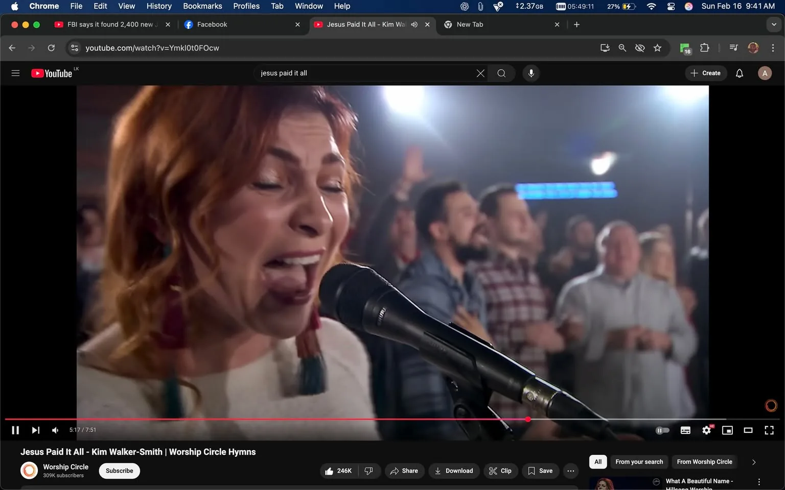 The image features a close-up of a woman singing into a microphone. She has medium-length, wavy hair that is reddish-brown and styled with loose curls. Her expression is intense and passionate, with her mouth open as she sings. She is wearing a light-colored, textured sweater, which appears cozy. Dangling from her ears are large, colorful earrings that add a pop of color to her outfit.

In the background, there are several people visible, some of whom are engaged in the performance. They appear to be in a worship setting, likely a concert or church event, as indicated by their expressions and body language. Some individuals are raising their hands, and others are smiling, suggesting a communal atmosphere of worship or celebration.

The lighting in the scene is bright, with a mix of warm and cool tones, creating a vibrant ambiance. There are blurred figures in the background, indicating a crowd, but they are not clearly defined. The setting appears to be indoors, possibly in a performance venue or church, with a stage or platform where the woman is performing.

At the bottom of the image, there is a YouTube video interface visible, indicating that this is a video titled "Jesus Paid It All - Kim Walker-Smith | Worship Circle Hymns." The video has a play bar showing the current time at 5:17 out of a total of 7:51 minutes. Below the video, there are options to subscribe, share, and download, along with a view count of 246K.

Overall, the image captures a moment of musical performance within a worship context, highlighting the singer's emotional engagement and the supportive crowd around her.