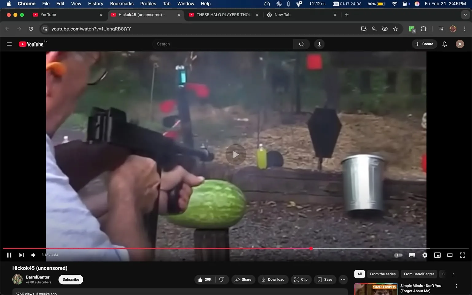 The image depicts a scene from a YouTube video titled "Hickok45 (uncensored)" on the platform. The video is hosted by a channel named "BarrelBanter," which has 49.8k subscribers. The video has garnered 676k views and was uploaded three weeks prior to the current date shown in the image.

In the foreground, a person is holding a firearm, which appears to be a semi-automatic weapon. The individual is positioned to the left side of the frame, with their face partially visible. They are wearing glasses and ear protection, which is orange in color. The person’s clothing consists of a light blue shirt, and their hands are gripping the firearm firmly, indicating they are preparing to shoot.

In front of the shooter, there is a green watermelon placed on a wooden platform, which is the target of the shot. The background features various shooting targets, including a black silhouette target and colored targets (red and yellow) hanging from a frame. The setting appears to be an outdoor shooting range, with gravel underfoot and a natural backdrop of trees and foliage.

The video player interface is visible at the bottom of the image, showing a play button and a timeline indicating the video is at 3 minutes and 19 seconds into a total length of 4 minutes and 53 seconds. The overall atmosphere suggests a recreational shooting activity, with an emphasis on target practice.