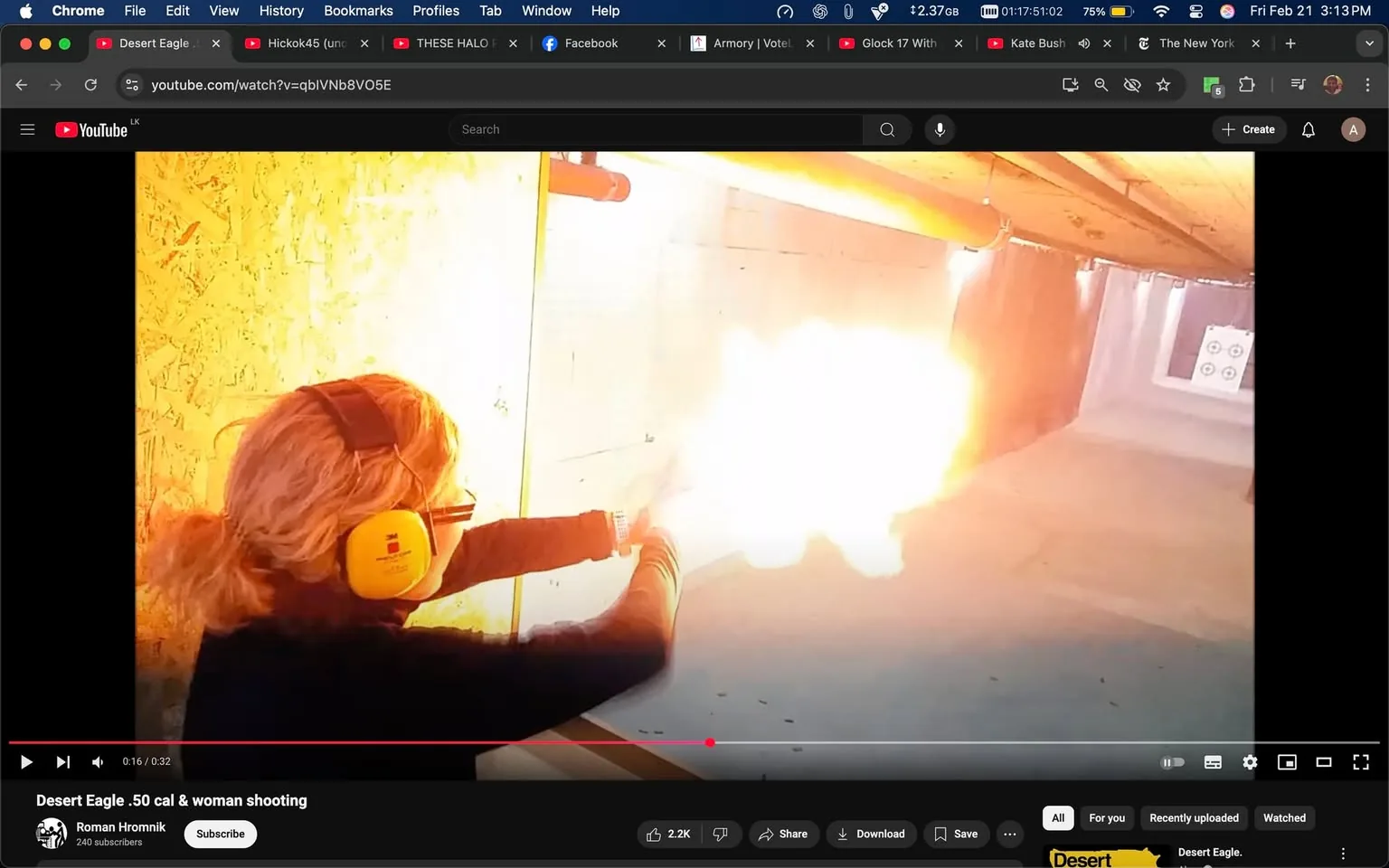 The image depicts a woman shooting a firearm in an indoor shooting range. She has shoulder-length, wavy blonde hair and is wearing yellow ear protection earmuffs. Her clothing consists of a black long-sleeve shirt. The woman is positioned to the left side of the image, aiming a handgun, which appears to be a Desert Eagle, towards a target located in the background.

The firearm is emitting a significant flash of fire from the muzzle, indicating that it has been discharged. The background features a concrete wall with a target visible further down the range. The target consists of concentric circles, likely used for aiming practice. The walls of the shooting range are made of concrete, and there are wooden beams visible above, suggesting a structured indoor environment.

The lighting in the image is bright, particularly around the area where the gun is fired, creating a stark contrast with the darker surroundings. There are no visible facial expressions due to the angle of the shot, but the focus is clearly on the action of shooting. 

In the upper part of the image, there is a YouTube interface visible, indicating that this is a still from a video titled "Desert Eagle .50 cal & woman shooting," uploaded by a user named Roman Hromnik. The video has a play bar showing a timestamp of 0:16 out of 0:32. Below the video, there are options to share, download, and save, along with a subscriber count of 240.

Overall, the image captures a moment of shooting practice in a controlled environment, highlighting both the action and the equipment involved.
