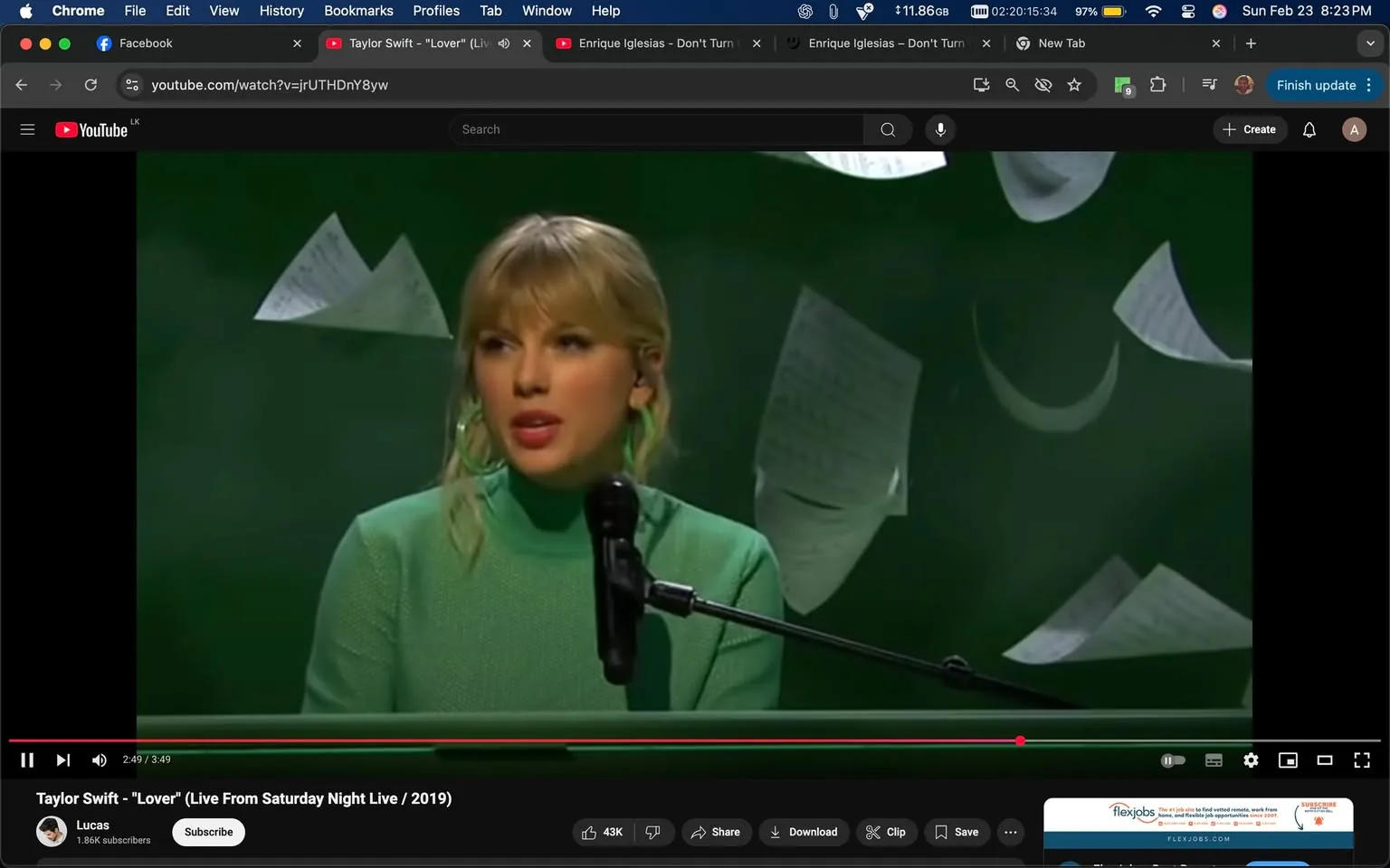 The image shows a scene from a performance, likely from a live television show. In the foreground, a woman is seated at a microphone. She has long, light blonde hair styled with bangs and is wearing a green, long-sleeved, high-neck sweater. Her makeup includes a bold lip color, and she is wearing large, circular green earrings that match her sweater. The expression on her face appears focused as she engages with the audience.

The microphone is positioned in front of her, and she is looking slightly to her left, suggesting she is either singing or speaking. Behind her, the background is a dark green color, which contrasts with her outfit. Scattered in the background are several sheets of paper, some of which appear to be partially crumpled or fluttering, indicating a dynamic atmosphere. The papers are white and may contain text, but the text is not legible in the image.

At the bottom of the image, there is a YouTube interface visible, indicating that this is a video. The title displayed is "Taylor Swift - 'Lover' (Live From Saturday Night Live / 2019)," suggesting that the woman in the image is Taylor Swift. The video is currently at 2 minutes and 49 seconds, with a total length of 3 minutes and 49 seconds. Below the video, there are options to subscribe, share, download, and clip the video, along with a subscriber count of 1.86K.

Overall, the setting appears to be a performance stage, likely during a live broadcast, with a focus on the artist and the musical performance.
