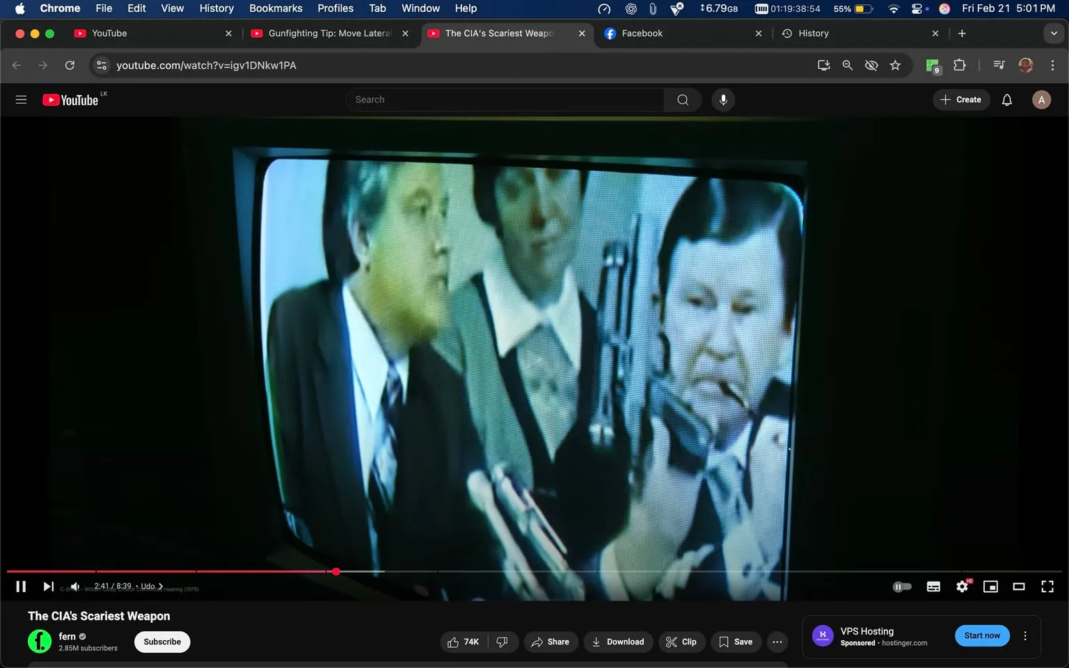 The image depicts a scene from a video, likely a news broadcast or documentary, displayed on a television screen. The screen shows three individuals engaged in a discussion. 

1. **Text and Logos**: 
   - At the bottom of the screen, there is a logo for "fern," which appears to be the name of the channel or production company. It is accompanied by the text "2.85M subscribers," indicating the channel's follower count. 
   - The video is titled "The CIA's Scariest Weapon," suggesting the content relates to a topic involving the CIA.

2. **People**:
   - **Left Individual**: A man in a dark suit and a light-colored shirt with a tie. He has short, dark hair and is speaking, looking towards the center of the frame. His expression appears serious.
   - **Center Individual**: A woman wearing a white blouse with a black vest or sweater over it. She has short, dark hair and is looking at the man on the left, seemingly engaged in the conversation.
   - **Right Individual**: Another man, dressed in a light-colored suit with a white shirt. He has dark hair and is holding a device that resembles a microphone or a radio. He appears to be listening intently, with a focused expression.

3. **Objects**:
   - The right individual is holding a device that looks like a communication tool, possibly a radio or microphone, which he is bringing close to his mouth.
   - There are several microphones positioned on the table in front of the individuals, indicating that this is likely a press conference or public discussion.

4. **Setting**:
   - The background is somewhat blurred, but it appears to be a formal setting, possibly an office or conference room. The lighting is dim, with a focus on the individuals in the foreground.
   - The television screen has a slight glare, making the image somewhat hazy, but the individuals and their actions are still discernible.

5. **Overall Context**:
   - The scene suggests a serious discussion, possibly related to national security or intelligence, given the title of the video and the presence of microphones, indicating a formal presentation or interview setting.

This description captures the observable details within the image without speculation or interpretation.