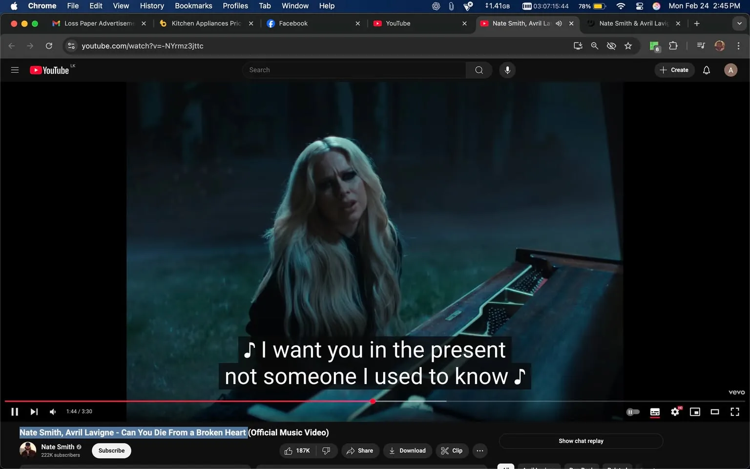 The image is a still from a music video displayed on a YouTube interface. The video features a woman with long, wavy blonde hair, who appears to be singing or performing. She is seated at a piano, which is positioned on the ground in a dimly lit outdoor setting. The background is dark, suggesting a nighttime environment, with blurred trees or foliage visible behind her, creating a moody atmosphere.

The woman is wearing a black outfit, which appears to be a long-sleeved top. Her facial expression seems to convey emotion, possibly reflecting the song's themes. The piano has a wooden finish, and the keys are partially visible, indicating it is an acoustic piano. The piano's lid is open, revealing the inner workings.

On the screen, there are subtitles displaying the lyrics: "I want you in the present not someone I used to know," which are prominently placed in a white font against a black background for clarity. The video title is visible at the bottom, reading: "Nate Smith, Avril Lavigne - Can You Die From a Broken Heart (Official Music Video)." Below this, there are details about the channel, including the name "Nate Smith" and the subscriber count of 222K. There are also interaction buttons such as "Subscribe," "Share," and "Download" visible beneath the video.

The overall color palette of the image is dark and muted, contributing to a somber or reflective mood. The lighting focuses on the woman and the piano, creating a spotlight effect in the otherwise shadowy environment. The interface elements of YouTube, including the play bar and video duration (3:30), are also visible, indicating the video is currently playing at 1:44.