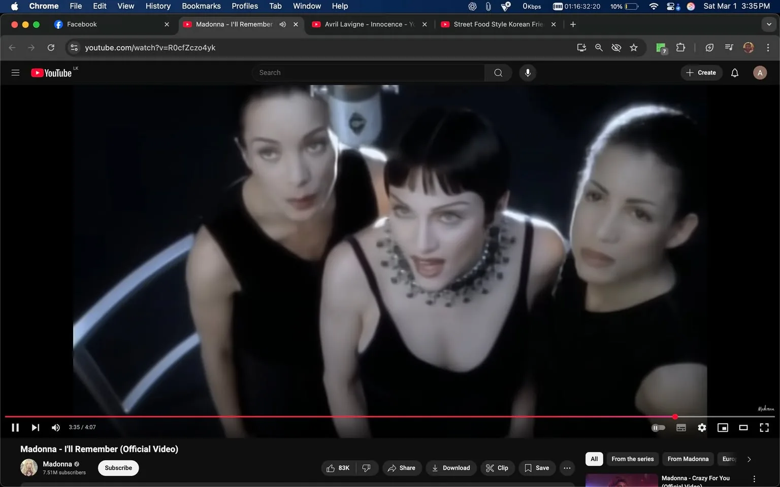 The image displays a scene from a music video featuring three women, all dressed in black attire. The setting appears to be a dimly lit environment with a dark background, which enhances the focus on the subjects. 

**Observable Details:**

1. **Text and Logos:**
   - At the bottom of the image, there is visible text indicating the video title: "Madonna - I'll Remember (Official Video)." The name "Madonna" is also displayed prominently, accompanied by a checkmark symbol indicating a verified account. Below this, there are statistics showing "83K" likes and options to share, download, or clip the video.

2. **People's Appearance:**
   - The woman in the center has short, dark hair styled in a bob. She is wearing a black sleeveless dress with a deep neckline and a statement necklace featuring large, dark stones. Her expression appears focused and engaged.
   - The woman on the left has long, dark hair pulled back into a sleek ponytail. She is wearing a similar black sleeveless outfit. Her expression is serious, and she is looking slightly upward.
   - The woman on the right also has long, dark hair, which is slicked back. She is wearing a black sleeveless top. Her expression is neutral, and she is gazing directly at the camera.

3. **Clothing:**
   - All three women are dressed in black, which creates a cohesive visual theme. The clothing is form-fitting and elegant, emphasizing their figures.

4. **Setting:**
   - The background is dark, with a soft glow that highlights the subjects. There is a circular light or reflective surface in the background, suggesting a studio or performance setting. The lighting creates a dramatic effect, focusing attention on the women.

5. **Facial Expressions:**
   - The expressions of the women range from engaged to serious, contributing to the overall mood of the scene.

Overall, the image captures a moment from a music video, showcasing the three women in a stylized, artistic presentation, with a focus on their attire and expressions against a dark, atmospheric backdrop.