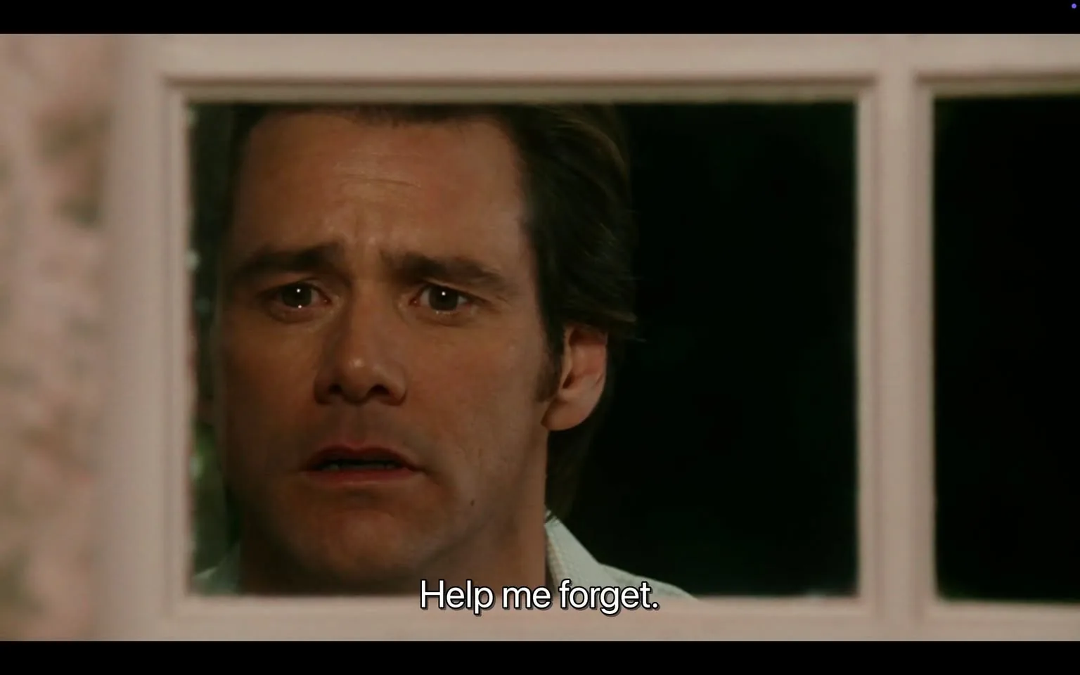 The image depicts a close-up of a man's face viewed through a window. He has a distressed expression, with his eyebrows furrowed and eyes wide, suggesting a sense of vulnerability or emotional turmoil. The man has short, dark hair with a slight wave, and he appears to be in his mid-30s to early 40s. His skin tone is fair, and he has a slight stubble on his face. 

He is wearing a light-colored shirt, which is partially visible, and the collar is turned down. The background is dark, indicating that it may be nighttime or in a dimly lit environment. The window frame is white, and the glass is clear, allowing a view of the man's face, which is the focal point of the image.

The text at the bottom of the image reads, "Help me forget," which is centered and in a simple, sans-serif font. The overall tone of the image conveys a moment of desperation or plea, but no further context is provided regarding the setting or situation.

There are no visible logos, brands, or other identifiable objects in the image. The focus remains solely on the man's expression and the window through which he is viewed. The background is blurred, emphasizing the subject's face and the emotional weight of the moment captured.