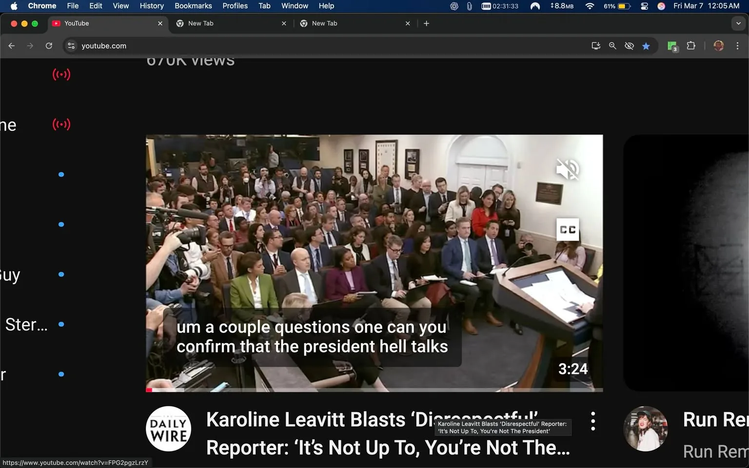 The image depicts a scene from a press briefing, likely held in a government building, given the presence of a podium and a backdrop that resembles the White House press room. 

In the foreground, there is a wooden podium with a dark surface, and papers are laid out on it. The podium is positioned in front of a large audience. A person, whose identity is not discernible, is standing behind the podium, possibly addressing the audience. 

The audience consists of a diverse group of individuals, primarily seated, with some standing at the back. The attendees are dressed in formal attire, including suits and blazers. Notably, a woman in the front row is wearing a green blazer over a white shirt, while another woman beside her is in a purple outfit. Several men are seen in suits, with varying colors such as gray and blue. 

In the background, there are framed pictures on the wall, which appear to be portraits or official photographs, but the details are not clear. The room is well-lit, with a mix of natural and artificial lighting, contributing to a professional atmosphere.

On the left side of the image, a camera is pointed towards the podium, indicating that the event is being recorded or broadcasted. There are also multiple individuals holding recording devices, suggesting a media presence.

At the bottom of the image, there is a caption that reads: "Karoline Leavitt Blasts ‘Disrespectful’ Reporter: ‘It’s Not Up To, You’re Not The President’," indicating the topic of discussion during the briefing. The video player interface is visible, showing options for playback and captions.

Overall, the setting is formal and indicative of a press conference, with a focus on communication between officials and the media.