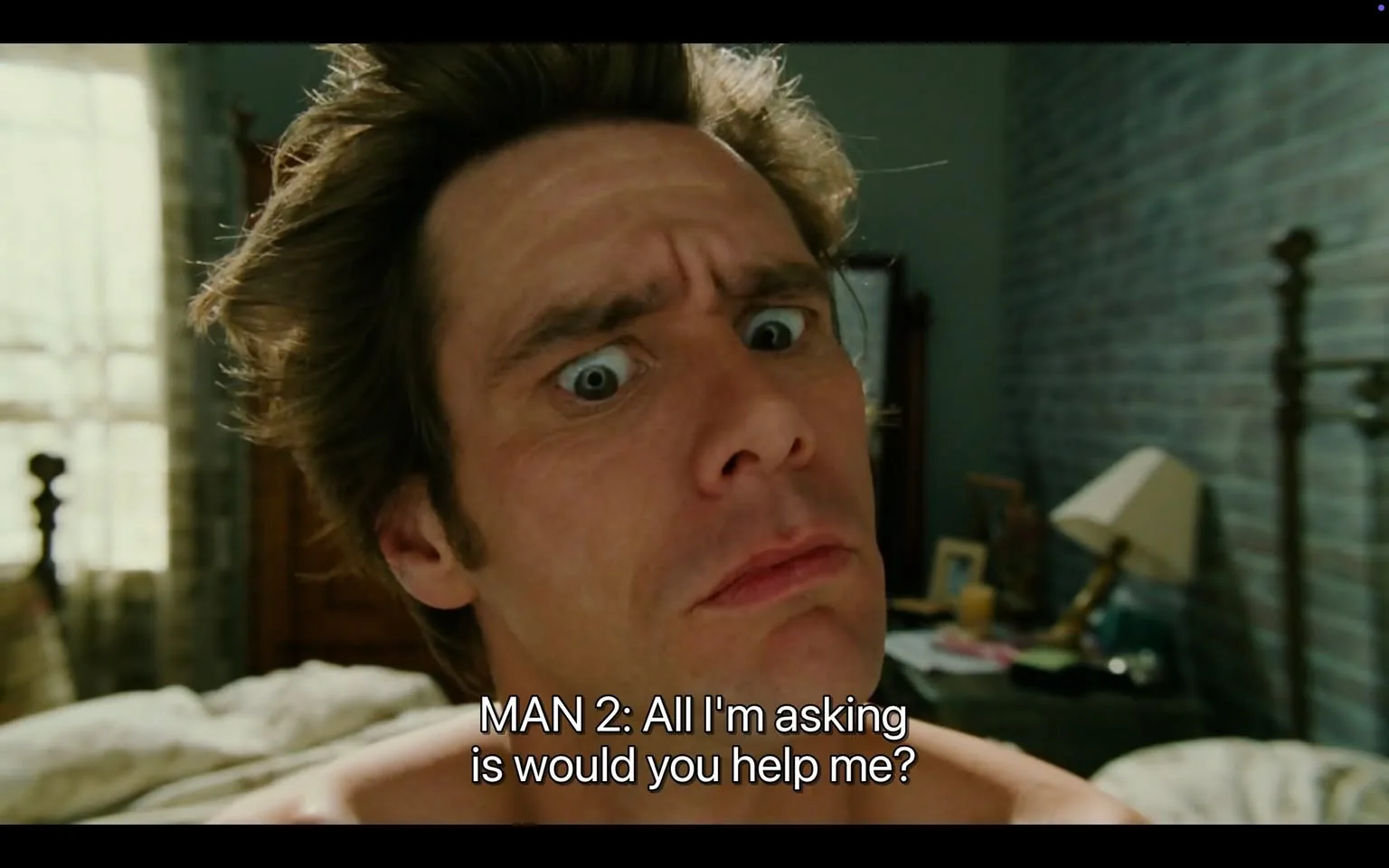 The image features a close-up of a man with a perplexed expression. He has tousled, light brown hair that appears somewhat unkempt, with strands sticking out in various directions. His facial features are exaggerated, with prominent furrows on his forehead and wide, expressive eyes that convey confusion or surprise. The man has a fair complexion and is shirtless, revealing a portion of his upper body.

In the background, there is a softly lit room with a window that has sheer curtains, allowing natural light to filter in. The walls are painted in a muted color, possibly light blue or gray, and there is a wooden bed frame visible behind him. On the bedside table, there are various items, including a lamp, a picture frame, and what appears to be a stack of papers or books, indicating a lived-in space.

The text overlay at the bottom of the image reads: "MAN 2: All I'm asking is would you help me?" This text is centered and appears in a bold, white font, contrasting with the darker background of the image.

Overall, the setting suggests a casual, possibly intimate environment, likely a bedroom, and the man's expression and the text imply a moment of dialogue or plea for assistance.