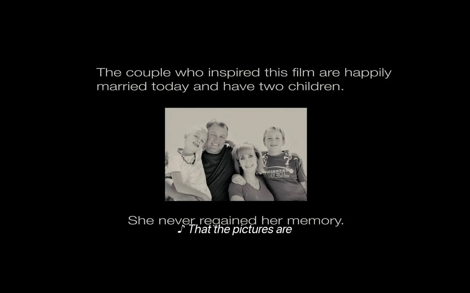 The image features a black background with white text and a central photograph. The text at the top reads: "The couple who inspired this film are happily married today and have two children." Below this, there is another line of text that states: "She never regained her memory." This line is followed by musical notes and the phrase "That the pictures are."

The photograph in the center is in black and white and depicts a family of four. The family consists of two children and two adults. The adults are positioned in the center, with the woman on the right and the man on the left. The woman has shoulder-length hair and is wearing a light-colored top. She is smiling and appears to be leaning slightly towards the man. The man has short hair and is wearing a dark shirt. He has a relaxed expression and is holding one of the children.

On the left side of the photograph, there is a young boy with short hair, wearing a striped shirt. He is leaning against the man, smiling. On the right side, there is another boy, also with short hair, wearing a dark shirt with the word "FUEL" printed on it. He is standing next to the woman, also smiling.

The overall composition of the image conveys a sense of family unity and happiness, with the text providing context about the couple's relationship and a hint of a narrative involving memory. The photograph is framed in a way that emphasizes the family, while the black background and white text create a stark contrast, drawing attention to the message being conveyed.