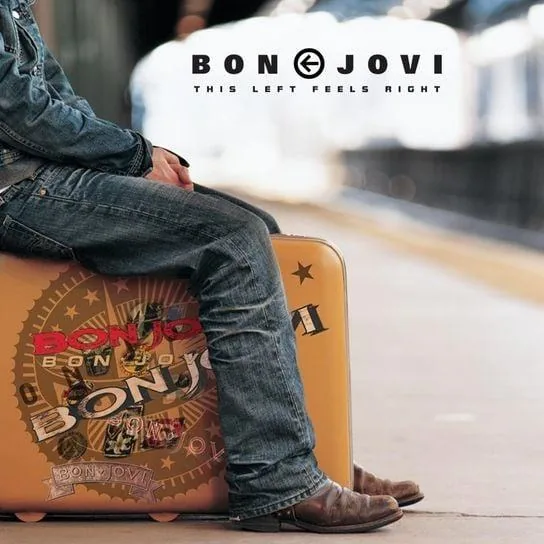 The image features a man sitting on a large, vintage-style suitcase. He is dressed in a denim jacket and blue jeans, with his legs crossed. The jeans appear to be slightly distressed, and he is wearing brown cowboy-style boots. His hands rest on his knees, and he has a relaxed posture. 

The suitcase is prominently displayed, featuring a design that includes the name "BON JOVI" in bold, stylized lettering. The suitcase is a light tan color and has various decorative elements, including a circular emblem with the name "BON JOVI" repeated in a circular pattern, along with other graphic designs that suggest travel or adventure.

In the background, there is a blurred setting that resembles a train station or platform, with soft lighting and a hint of movement, indicating that it may be a busy area. The overall color palette of the image is warm, with earthy tones dominating the scene.

At the top of the image, there is text that reads "BON JOVI" in large letters, followed by the phrase "THIS LEFT FEELS RIGHT" in smaller text. The font is modern and bold, contributing to the overall aesthetic of the image.

The focus is primarily on the man and the suitcase, with the background serving to enhance the context of travel or waiting. The image conveys a sense of nostalgia and adventure, with the branding clearly associated with the musical group Bon Jovi.