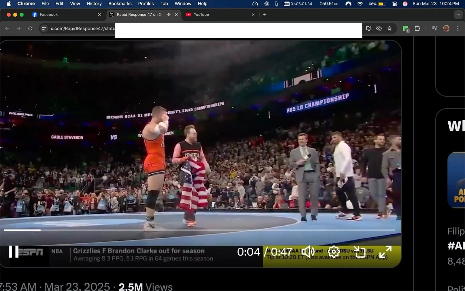 The image depicts a wrestling match taking place in a large arena filled with spectators. The setting appears to be a championship event, likely the NCAA Division I Men's Wrestling Championships, as indicated by the text displayed in the background. 

In the foreground, two wrestlers are present on a circular blue mat. One wrestler, wearing an orange singlet with black accents, is raising his arm in a celebratory gesture, possibly indicating victory. He has a muscular build and short hair. The other wrestler, dressed in a red and white striped singlet, is holding an American flag and appears to be in a more subdued posture, possibly acknowledging the crowd or the event.

To the right of the wrestlers, a man in a gray suit is holding a microphone and appears to be speaking or announcing something. He has short hair and is looking towards the wrestlers. There are additional individuals in the background, some of whom are dressed in casual attire, indicating a mix of participants and spectators.

The crowd is visible in the background, with many people standing and cheering, creating a lively atmosphere. The arena is well-lit, with colorful lights illuminating the space. Various banners and signs can be seen, including one that reads "205 LB CHAMPIONSHIP," further confirming the nature of the event.

Overall, the image captures a moment of excitement and celebration in a competitive sports environment, with a focus on the wrestlers and the surrounding audience.
