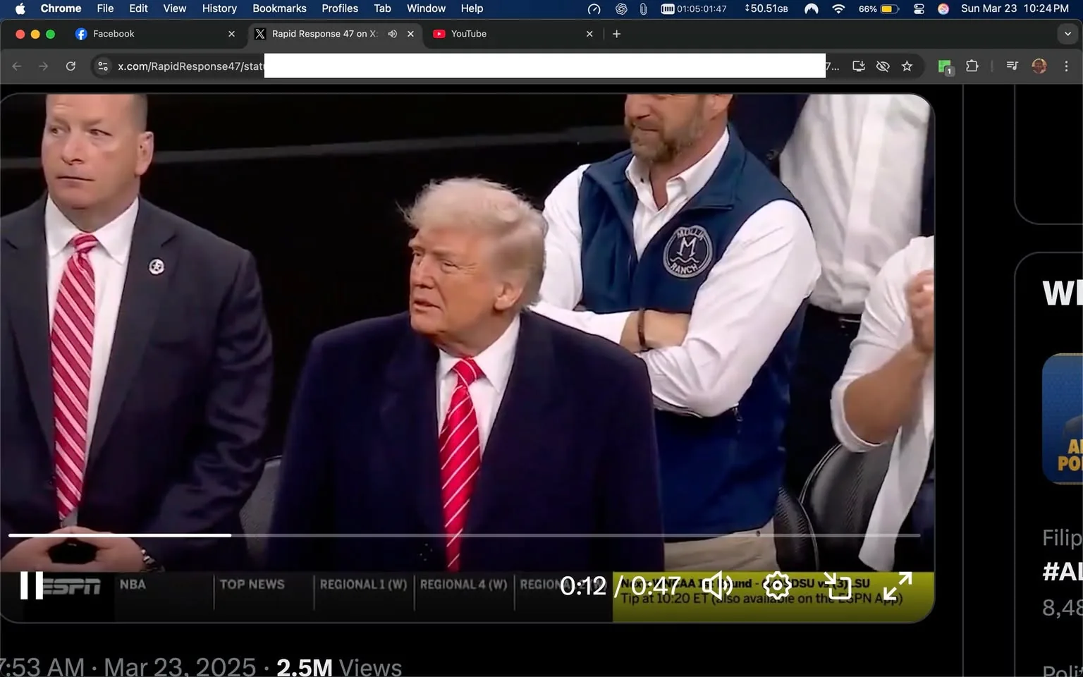 The image depicts a group of individuals at a public event, likely a sports game, given the context of the surrounding posts. 

In the foreground, there are three men. The man on the left is wearing a dark suit with a white shirt and a red striped tie. He has a serious expression and is looking to the right. Next to him is another man in a dark suit, also with a white shirt and a red striped tie. He appears to be focused on something in front of him, possibly the event or the crowd. 

The third man, who is possibly a public figure, has light-colored hair styled back and is wearing a dark coat over a white shirt. He has a red striped tie and is looking to his left, appearing engaged in the event. His expression is neutral, and he seems to be observing the surroundings. 

In the background, there are additional individuals, including a man wearing a blue vest over a white shirt, with his arms crossed. Another person is partially visible, wearing a white shirt and clapping. The setting appears to be indoors, likely in a stadium or arena, with a dark backdrop that suggests a large crowd is present. 

There are no visible signs, logos, or product labels in the image. The overall atmosphere seems to be one of anticipation or excitement, typical of a sports event. The lighting is bright, highlighting the individuals in the foreground. 

The image captures a moment of observation and engagement among the attendees, with a focus on the individuals in the foreground.