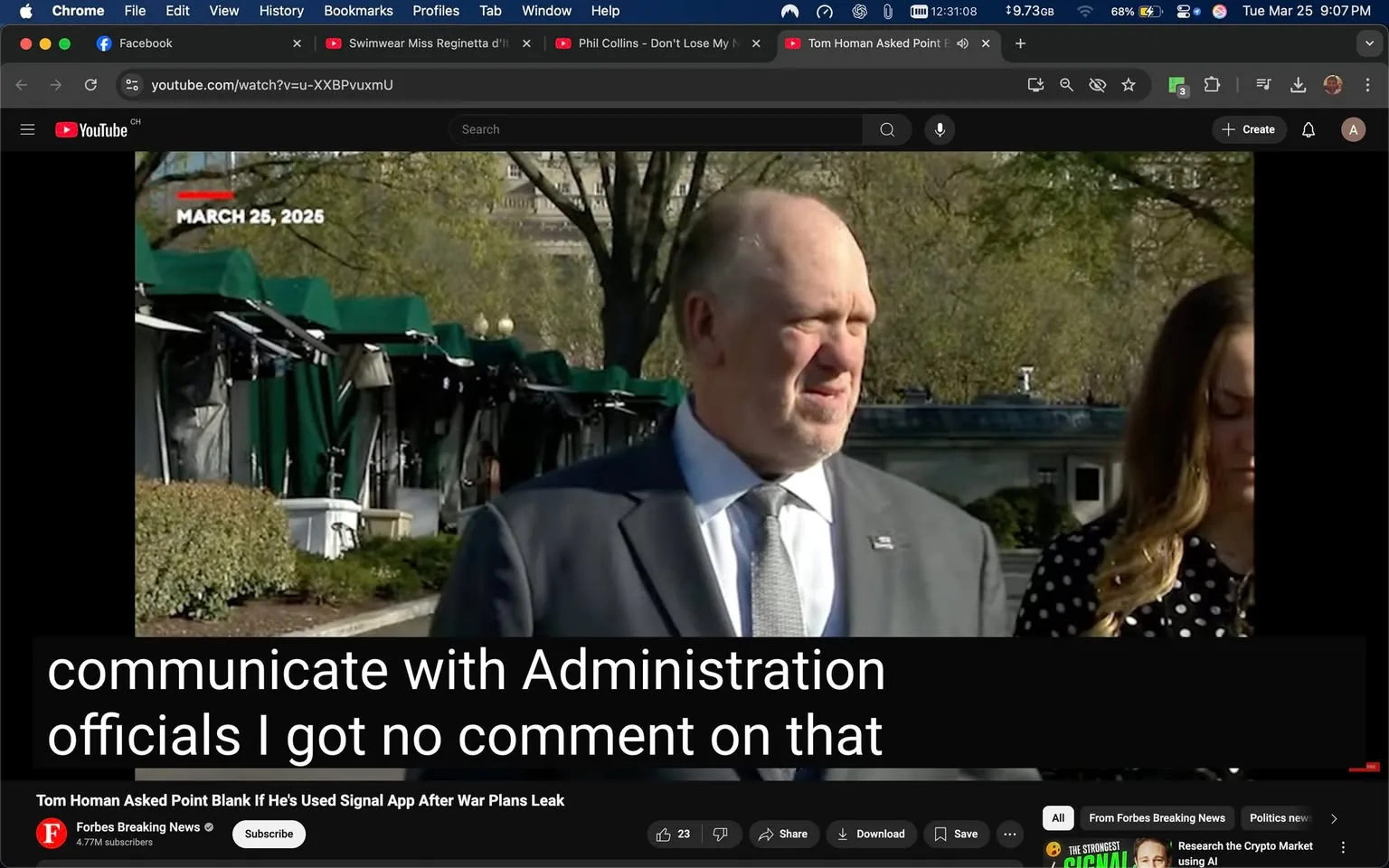 The image shows a scene outdoors, likely at a press event or public appearance. In the foreground, there are two individuals: a man and a woman. 

The man is wearing a dark suit with a light blue dress shirt and a silver tie. He has a bald head with some gray hair on the sides and appears to be in his late 40s to early 50s. His expression seems neutral, and he is looking slightly to the right, possibly engaged in conversation or responding to a question. 

The woman next to him has long, wavy brown hair and is wearing a black dress with white polka dots. She appears to be looking down, possibly distracted or contemplative. 

In the background, there are several green canopies, which suggest that this event might be taking place in a park or outdoor venue. There are also some trees with budding leaves, indicating that it is likely springtime. 

At the top of the image, there is a date displayed: "MARCH 25, 2025." Below the individuals, there is a caption that reads: "communicate with Administration officials I got no comment on that." This text appears to be a transcription of what the man might be saying during the event.

The bottom of the image features a YouTube interface, indicating that this is a video still. There are various buttons for interaction, such as "Subscribe," "Share," and "Download," along with a view count and a comment section. The logo for "Forbes Breaking News" is also visible, suggesting that this content is related to news coverage.

Overall, the scene captures a moment of public discourse, likely related to political or administrative matters, in a formal outdoor setting.