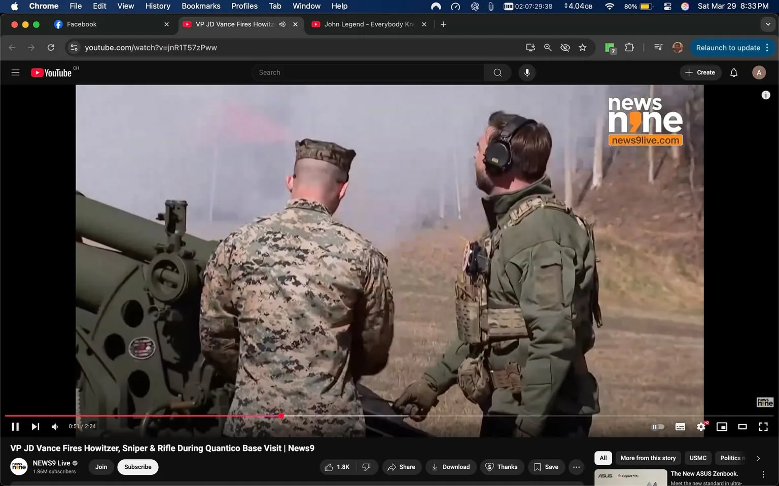 The image depicts a military setting where two individuals are engaged in an activity related to artillery. 

1. **People**: 
   - There are two men visible in the foreground. 
   - The man on the left is wearing a military camouflage uniform, which includes a jacket with a pattern typical of U.S. Marine Corps attire. His hair is short and he is facing slightly away from the camera, looking towards the right.
   - The man on the right is dressed in a green tactical jacket and appears to be wearing a headset or ear protection. He has a short hairstyle and is looking upwards, possibly observing something in the distance or reacting to a sound.

2. **Clothing and Gear**: 
   - The man in camouflage has a standard military cut and is wearing a utility belt. 
   - The man in the tactical jacket has additional gear, including a tactical vest with pouches, suggesting he may be involved in operational duties.

3. **Setting**: 
   - The background shows a field with some trees in the distance, indicating an outdoor training or demonstration area. 
   - There is a large artillery piece (howitzer) visible on the left side of the image, which is pointed towards the right. The artillery is green and appears to be in a ready position for firing.
   - There is smoke or mist in the air, likely from a recent firing or demonstration, creating a dynamic atmosphere.

4. **Environmental Context**: 
   - The scene suggests a military exercise or demonstration, possibly involving the firing of the howitzer. 
   - The presence of smoke indicates recent activity, and the individuals appear to be part of a training or operational team.

5. **Text and Logos**: 
   - In the top right corner, there is a logo that reads "news9live.com," indicating that this image may be part of a news broadcast or report. 
   - The video player interface is visible at the bottom, showing controls typical of a YouTube video, including options to like, share, and save.

Overall, the image captures a moment in a military exercise, highlighting the equipment and personnel involved in such activities.