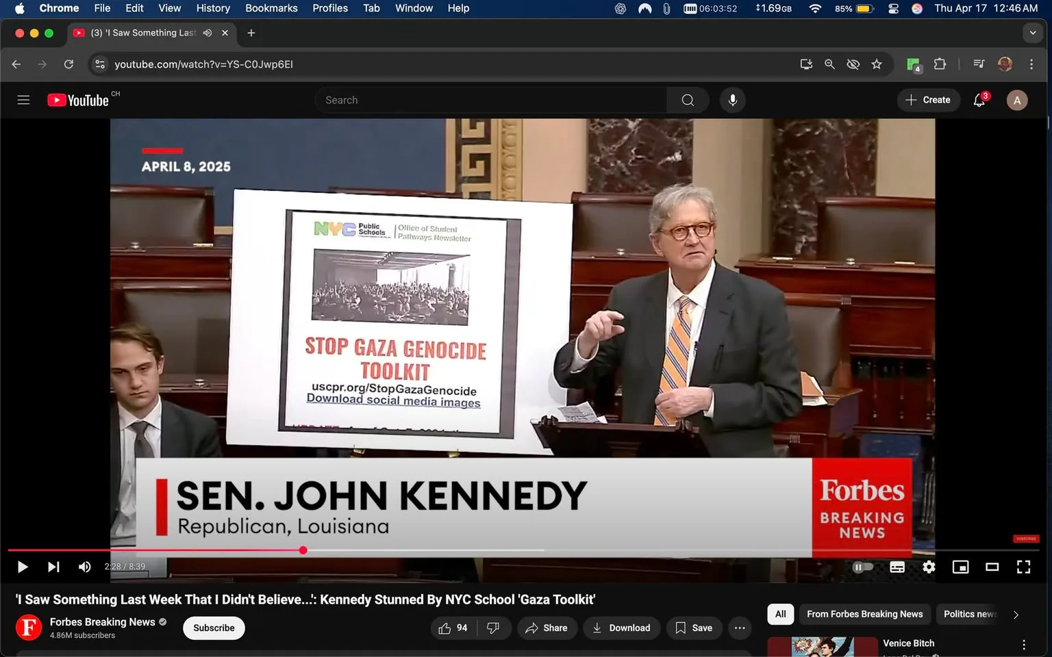 The image depicts a scene from a Senate session, dated April 8, 2025. A man, identified as Senator John Kennedy, is standing at a podium in the Senate chamber. He is wearing a dark suit with a white shirt and a striped tie that features orange and blue colors. His hair is gray and styled in a neat manner. He is gesturing with his right hand while holding a piece of paper or a pointer in his left hand, indicating a level of engagement in his speech.

Behind him is a large poster or sign that reads "STOP GAZA GENOCIDE TOOLKIT" in bold red letters. The sign also includes the logo of NYC Public Schools at the top, along with the text "Office of Student Pathways Newsletter." Below the main headline, there is a web address: "uscpr.org/StopGazaGenocide," and a note to "Download social media images." The poster features a black-and-white image of a crowd, likely related to the topic being discussed.

In the foreground, there is another individual seated, appearing to be a young man in a suit, who looks somewhat disengaged or contemplative, with his head slightly down and a neutral expression on his face.

The setting is the interior of the Senate chamber, characterized by dark wood paneling and a formal atmosphere. The background includes rows of empty seats, indicating that the chamber may not be fully occupied at the moment. The overall lighting is bright, typical of a legislative environment.

The lower part of the image features a banner with the text "SEN. JOHN KENNEDY" and "Republican, Louisiana," indicating his political affiliation and state representation. The banner is styled in a way that suggests it is part of a news broadcast, possibly from Forbes Breaking News, as indicated by the logo in the bottom right corner. 

Overall, the image captures a moment of political discourse, focusing on a significant topic related to Gaza, with visual elements that emphasize the formal nature of the Senate proceedings.