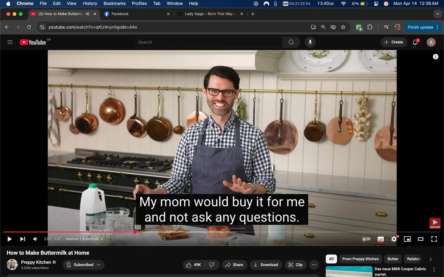 The image shows a kitchen setting where a person is presenting a cooking demonstration. The individual is wearing a checkered shirt, with the colors being predominantly white and dark blue, and an apron that is dark gray. They have glasses and a friendly smile, indicating a welcoming demeanor. The person is gesturing with their hands, possibly explaining a point or engaging with an audience.

In the background, there are several copper pots and pans hanging from a brass rod, which adds a classic touch to the kitchen decor. The kitchen features a large stove with multiple burners, and the cabinetry is a light color, likely white or cream. There are decorative plates displayed on the wall above the stove, contributing to the aesthetic of the kitchen.

On the countertop, there are various items visible: a clear glass measuring cup, a bottle, and a carton of milk with a green cap, indicating it may be whole milk. There is also a bowl that appears to contain a mixture, possibly for the recipe being discussed. The text overlay on the video reads, "My mom would buy it for me and not ask any questions," suggesting a light-hearted or nostalgic commentary related to the cooking process.

The overall atmosphere of the kitchen is bright and inviting, with natural light illuminating the space. The setting appears to be a home kitchen, designed for cooking demonstrations or tutorials.