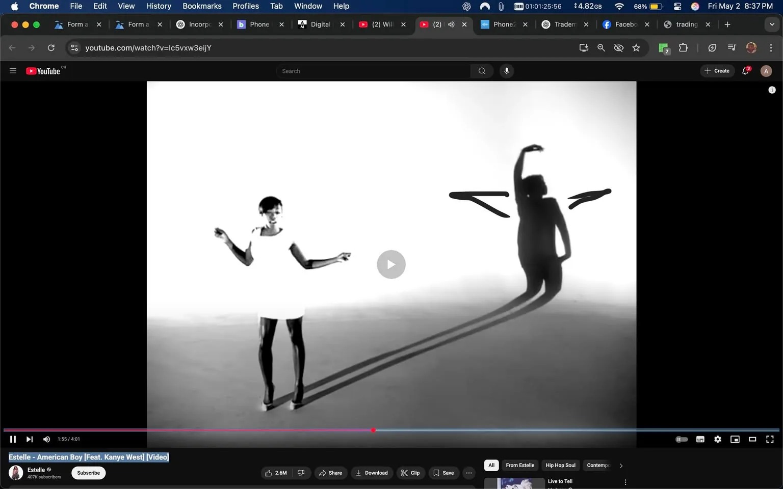 The image displays a scene from a music video on YouTube, specifically for the song "American Boy" by Estelle featuring Kanye West. The video is presented in black and white. 

In the foreground, a woman is dancing. She is wearing a short, white dress and high heels. Her hair is styled short and appears to be dark. The woman has her arms raised, with one hand bent at the elbow and the other extended outward. Her facial expression is not clearly visible due to the monochrome effect, but she appears to be engaged in the dance.

To the right of the woman, a shadow is cast on the background, which is a light gray or white. The shadow depicts a figure with arms raised, creating a dynamic visual contrast. The shadow appears to be elongated, suggesting a light source positioned in front of the dancer.

The background is minimalistic, with a smooth, light surface that lacks any distinct features or objects, emphasizing the dancer's movements. The overall composition focuses on the interplay between the dancer and her shadow, creating a visually striking effect.

At the bottom of the image, there is a YouTube interface visible, including the video playback controls, a play button, and a progress bar indicating the video is at 1 minute and 55 seconds out of a total of 4 minutes and 1 second. Below the video, there are options to subscribe, share, download, clip, and save, along with a channel name "Estelle" and a subscriber count of 407K. The video has a view count of 2.6 million, indicating its popularity.

No additional text, logos, or identifiable brands are present in the image apart from the YouTube branding. The overall aesthetic is sleek and modern, focusing on the artistic representation of dance and shadow.