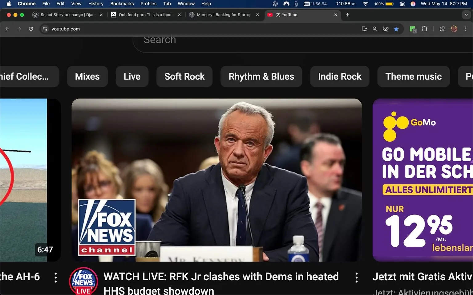 The image displays a screenshot of a YouTube interface. The background is dark, consistent with a typical YouTube dark mode setting. 

In the center of the image, there is a prominent figure, a man with gray hair styled back, wearing a dark suit and a white shirt with a tie. He has a serious expression on his face, appearing to be in a formal setting, possibly during a hearing or testimony. The man is seated at a table with a nameplate that reads "Mr. Kennedy." In the background, there are blurred figures of other individuals, including two women with light-colored hair, suggesting they are also in the same setting.

To the left of the central figure, there is a logo for "Fox News Channel," prominently displayed in blue and white. Below this logo, there is text that reads, "WATCH LIVE: RFK Jr clashes with Dems in heated HHS budget showdown," indicating that this is a live broadcast or segment related to a political event.

On the right side of the image, there is an advertisement for a mobile service provider, "GoMo," featuring a purple background with yellow circles and text that states, "GO MOBILE IN DER SCHWEIZ ALLES UNLIMITIERT NUR 12,95 /Mt. lebenslang," which translates to "GO MOBILE IN SWITZERLAND UNLIMITED EVERYTHING ONLY 12.95 / month for life."

The bottom of the image shows a video thumbnail with a red circle around a helicopter, labeled with a duration of "6:47." 

Overall, the image captures a moment from a political broadcast, highlighting a significant figure in a serious context, alongside promotional content typical of a digital media platform.