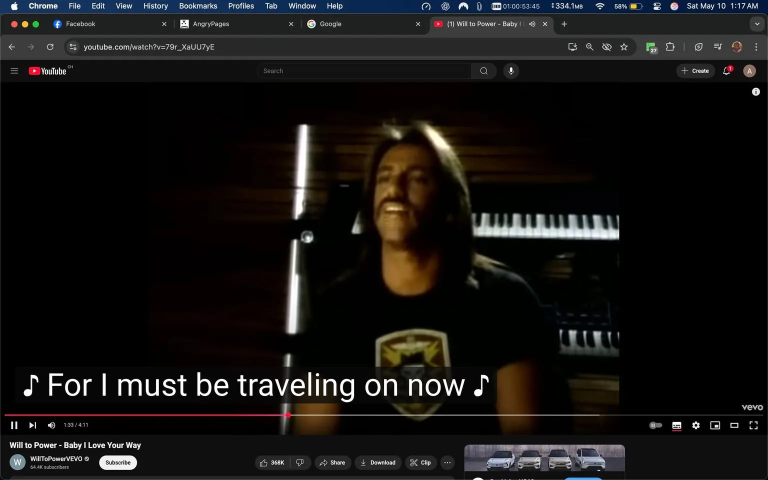 The image is a still from a music video, likely featuring a male performer. He has long, dark hair and a mustache, and he is wearing a black t-shirt with a shield-like emblem on it, which appears to have a design that includes a star and possibly some stripes. The background is dimly lit, with wooden panels visible, suggesting an indoor setting. 

In the background, there is a keyboard or piano, with keys partially visible, indicating a musical context. The performer is facing the camera, smiling, and appears to be singing or expressing emotion related to the lyrics, which are displayed on the screen as subtitles. The text reads, "For I must be traveling on now," indicating that the song is likely about movement or change.

The video interface shows that it is playing on YouTube, with the title "Will to Power - Baby I Love Your Way" displayed at the bottom. There are also viewer engagement metrics, including a view count of 368K and a subscriber count of 64.4K for the channel "WillToPowerVEVO." The video controls are visible at the bottom, including options to share, download, and clip the video.

Overall, the setting is intimate and focused on the performer, with an emphasis on the musical elements and the emotional delivery of the song. The lighting and background contribute to a nostalgic or reflective atmosphere, typical of music videos from the era.