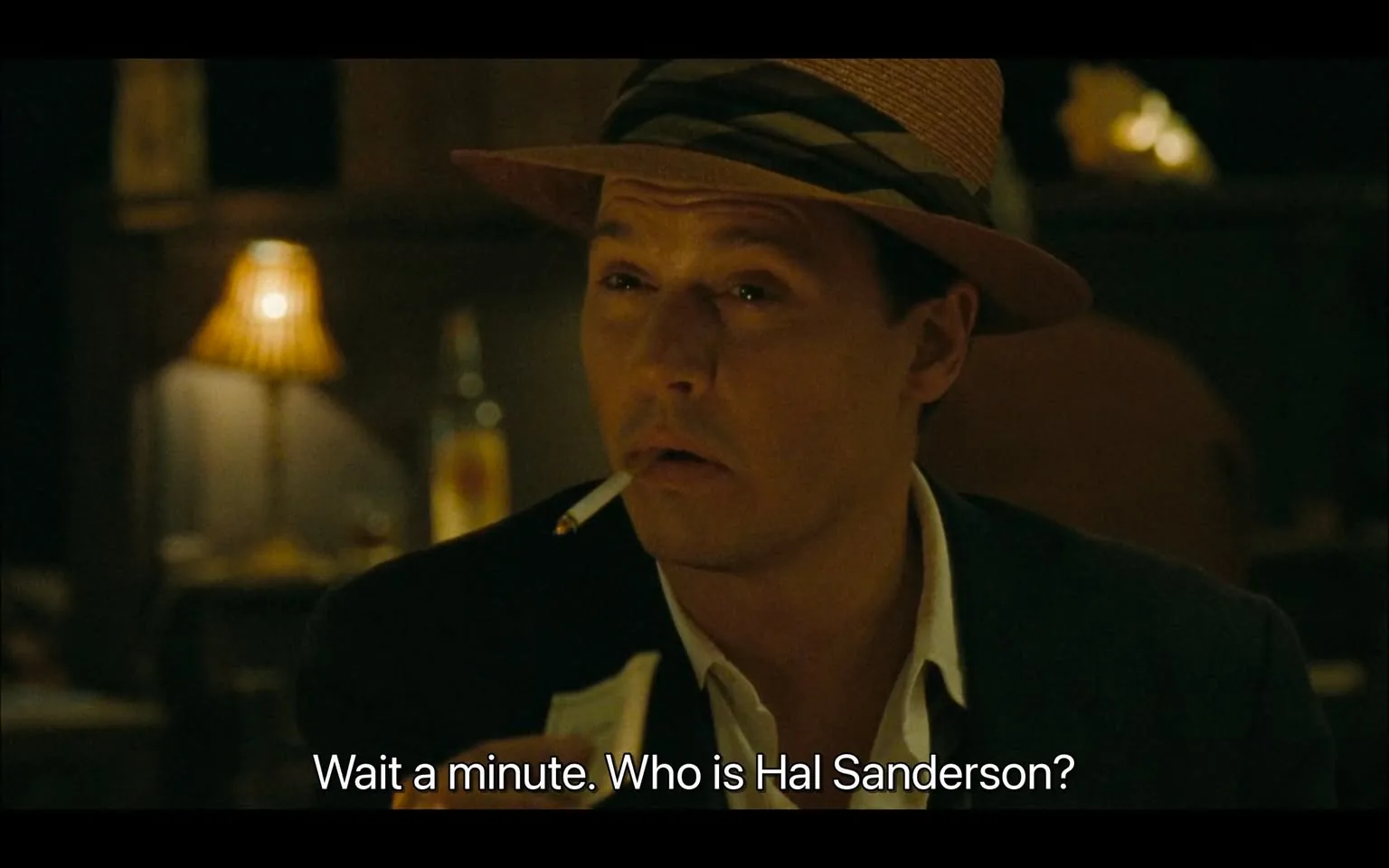 The image features a man seated at a table in a dimly lit setting, likely a bar or restaurant. He has a cigarette in his mouth and is wearing a straw hat with a dark band around it. His attire includes a dark jacket over a white shirt, which is partially unbuttoned at the collar. The man has a slightly furrowed brow and a contemplative expression, suggesting he is engaged in thought or conversation.

In the background, there are warm, ambient lights, including a lamp with a pleated shade that casts a soft glow. A bottle is visible on the table behind him, although the label is not clearly discernible. The overall atmosphere appears relaxed and intimate, typical of a social setting.

The text overlay at the bottom reads: "Wait a minute. Who is Hal Sanderson?" This indicates that the man is likely involved in a dialogue or narrative context, but no additional context about the conversation is provided in the image.

The background is somewhat blurred, focusing attention on the man and his expression. The color palette is warm, with browns and soft yellows dominating the scene, contributing to the cozy ambiance. The setting does not provide any specific indicators of time or place beyond the general bar or restaurant environment.