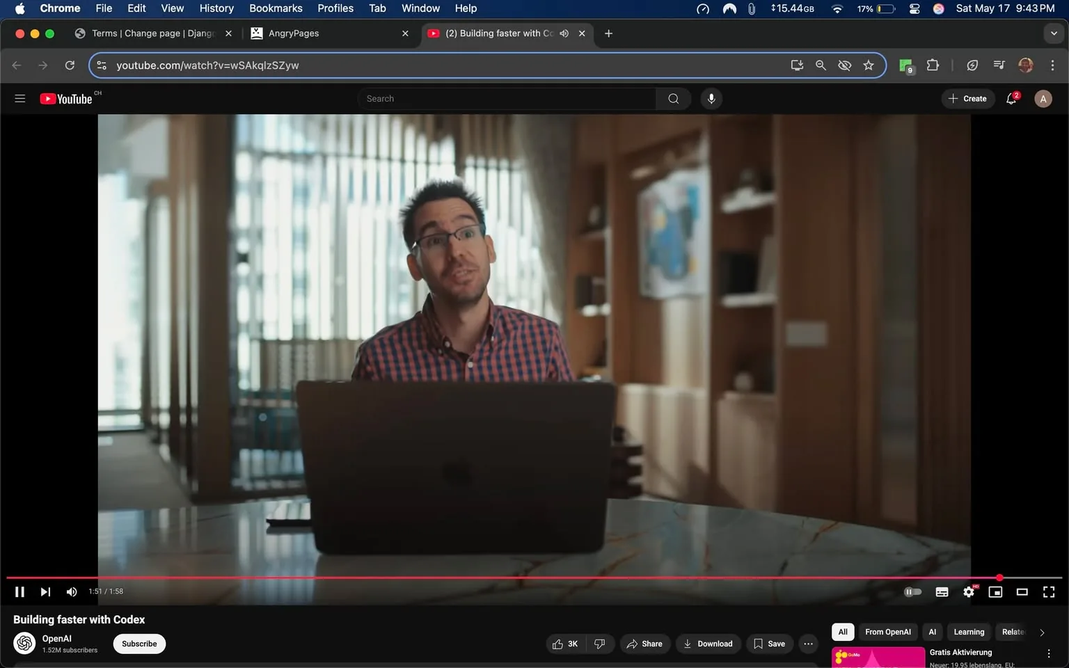 The image features a man sitting at a table with a laptop in front of him. He appears to be engaged in a conversation or presentation. The man has short, dark hair styled in a slightly messy manner and is wearing rectangular glasses. He is dressed in a red and blue checkered shirt, which is buttoned up to the collar. His expression is animated, suggesting he is speaking or explaining something.

The laptop on the table is a MacBook, identifiable by its sleek design and the Apple logo on the back. The table itself has a marble surface with visible veining, adding a touch of elegance to the setting. 

In the background, there are large windows with vertical blinds that allow natural light to filter through, creating a bright atmosphere. The walls are decorated with wooden panels, and there are shelves with various items, including books and decorative objects. A piece of artwork is visible on the wall, featuring abstract shapes and colors, which adds to the modern aesthetic of the space.

The overall setting appears to be a contemporary office or a well-designed home workspace, characterized by a clean and organized look. The lighting is warm and inviting, contributing to a professional yet relaxed environment. The video playback controls are visible at the bottom of the screen, indicating that this is a YouTube video titled "Building faster with Codex," with a duration of 1 minute and 58 seconds. The video is from OpenAI, as indicated by the channel name and subscriber count displayed on the screen.